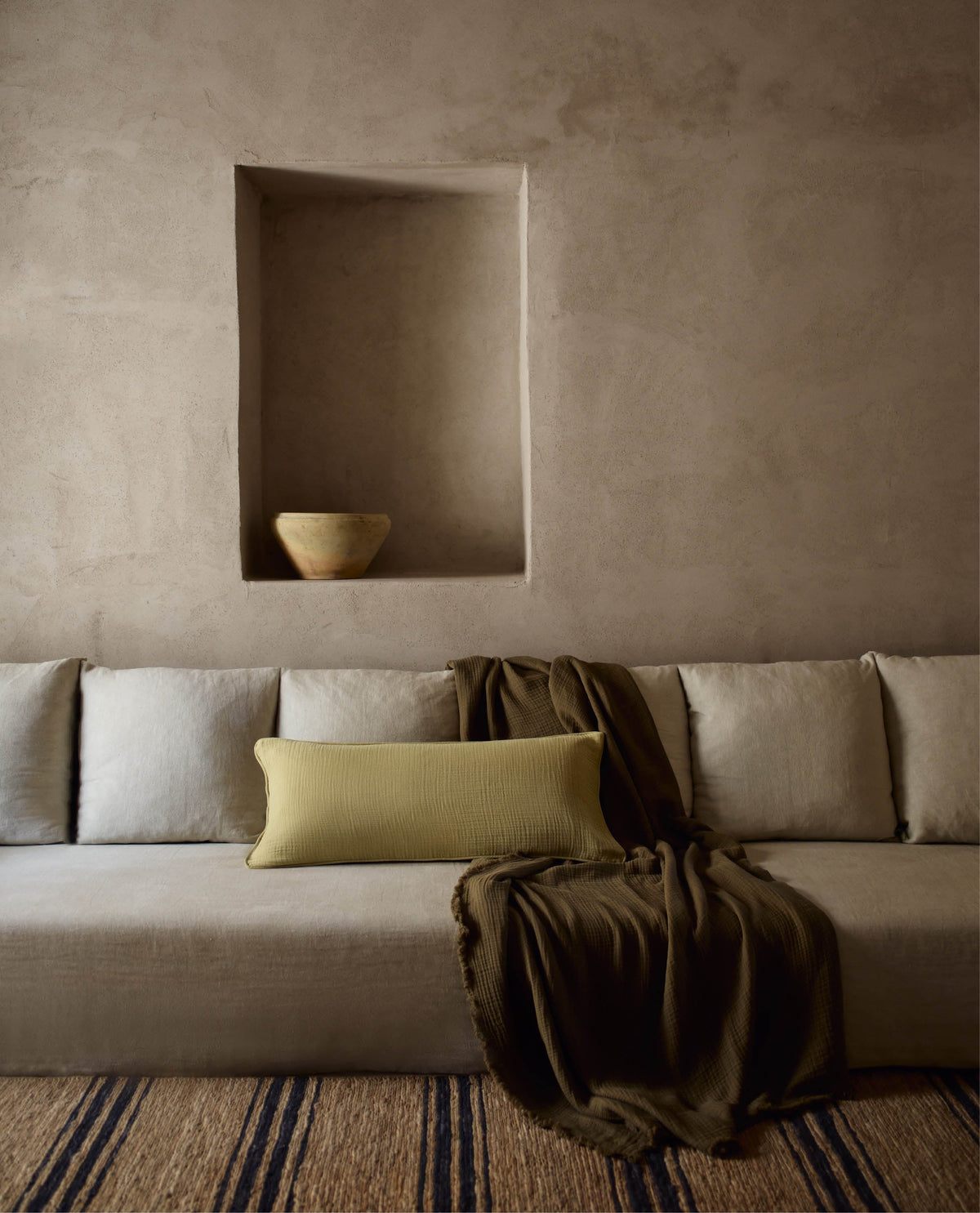 A brown velvet cotton throw with a light green cotton muslin lumbar cushion placed on a long beige sofa