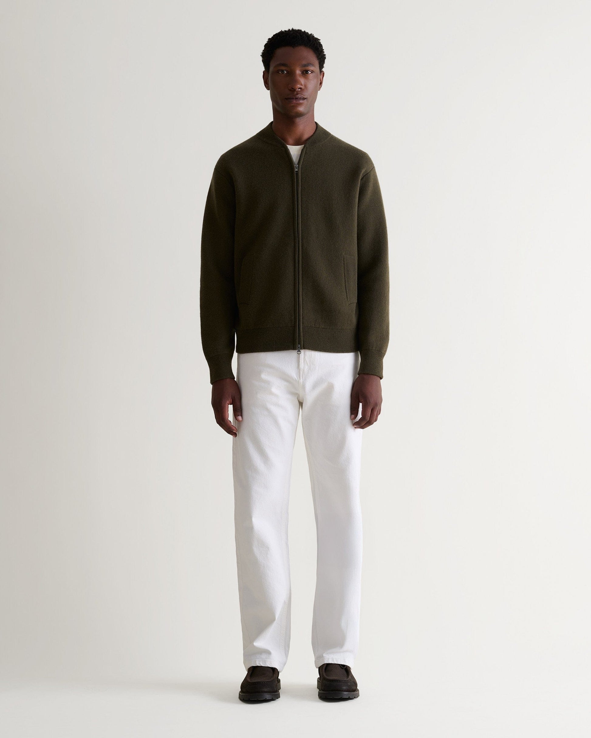Full length of man wearing dark green cashmere merino double-faced knitted bomber jacket with white T-shirt and jeans.