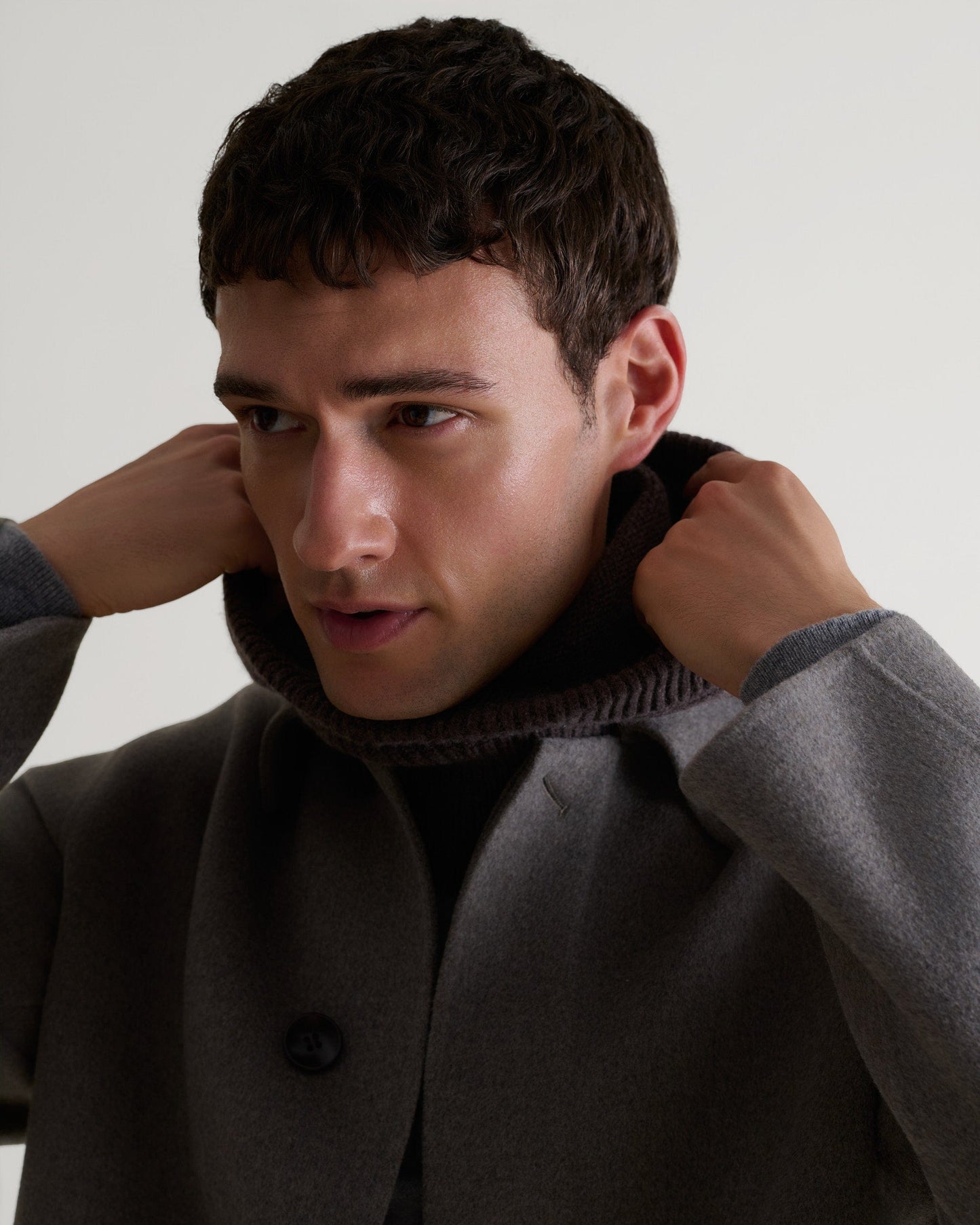 Close up of man wearing Rise & Fall's fawn coloured cashmere merino double-faced wool coat. Worn with grey cashmere hoodie.