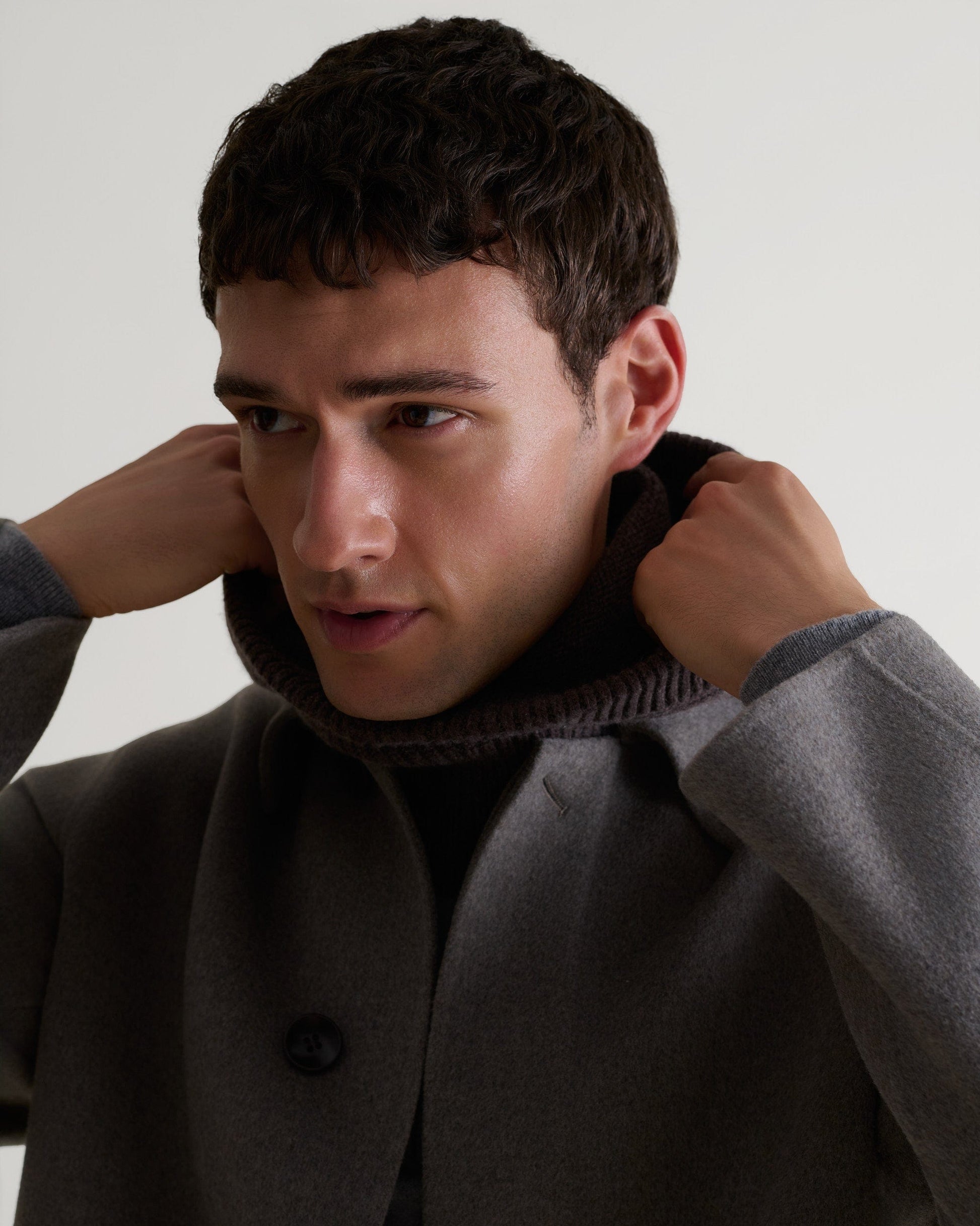Close up of man wearing Rise & Fall's fawn coloured cashmere merino double-faced wool coat. Worn with grey cashmere hoodie.