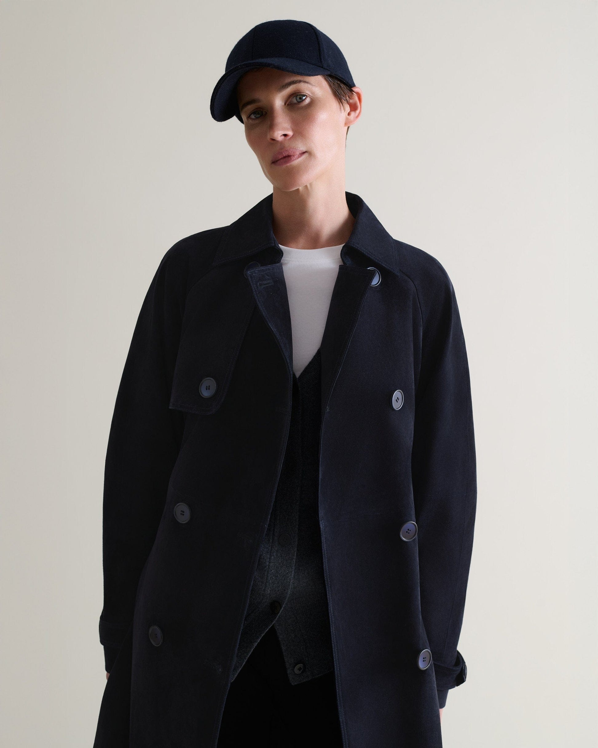 Front view of woman wearing navy cashmere merino wool baseball cap with matching suede trench coat and a white t-shirt.