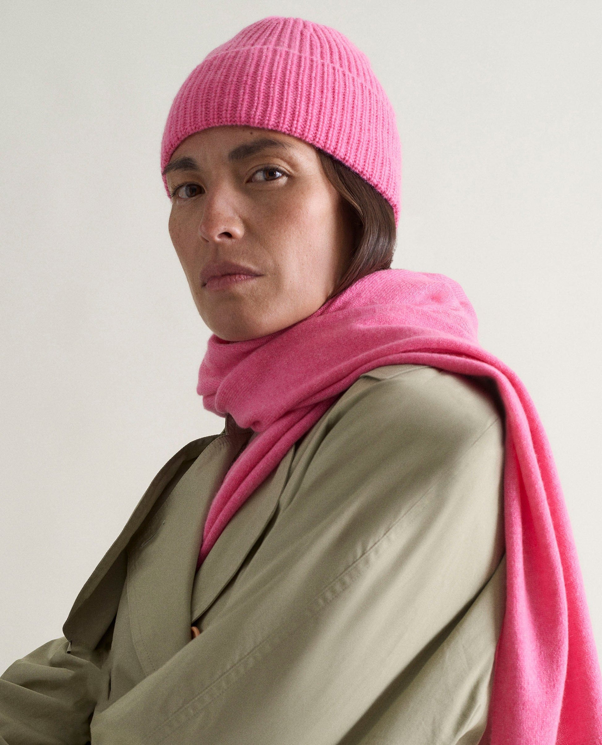 Image 1 of 2 showing woman wearing Rise & Fall's women's finest cashmere scarf in pink with matching beanie and beige trench coat.