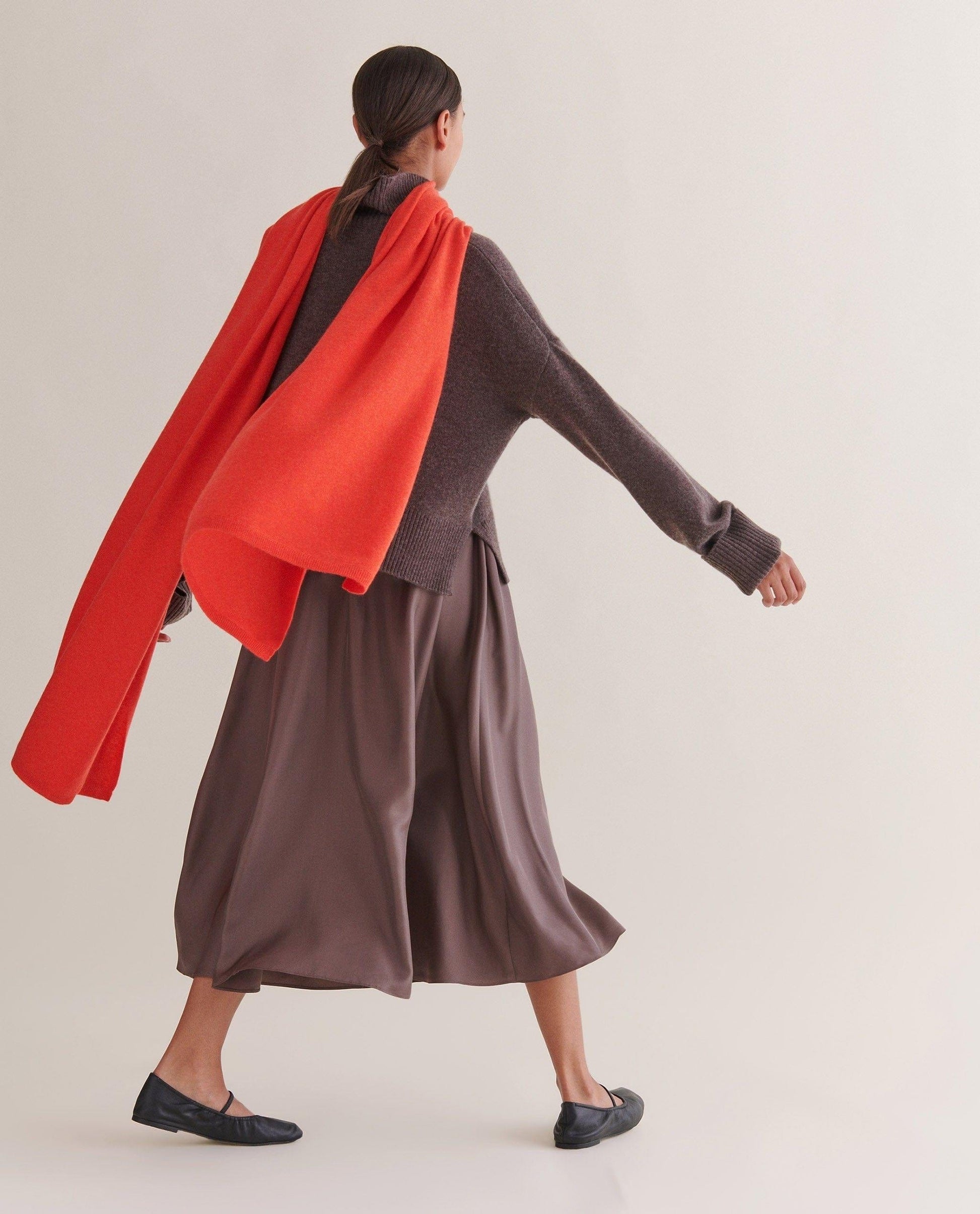 Image 1 of 2 showing woman wearing Rise & Fall's oversized cashmere scarf with chocolate jumper and silk skirt, colour: poppy red