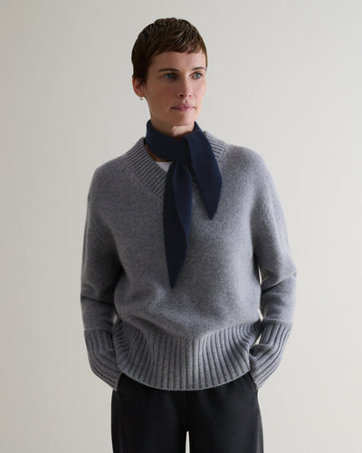 Image 1 of 2 showing woman wearing Rise & Fall's navy fine cashmere ribbed micro bandana with grey v-neck jumper, black trousers, white t-shirt.