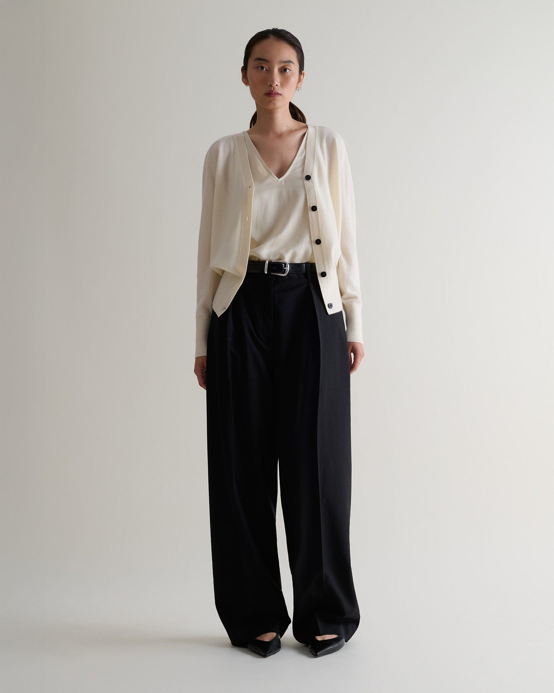Image 1 of 3 showing woman wearing Rise & Fall's buttermilk fine cashmere blouson cardigan with matching top and black wide leg trousers.