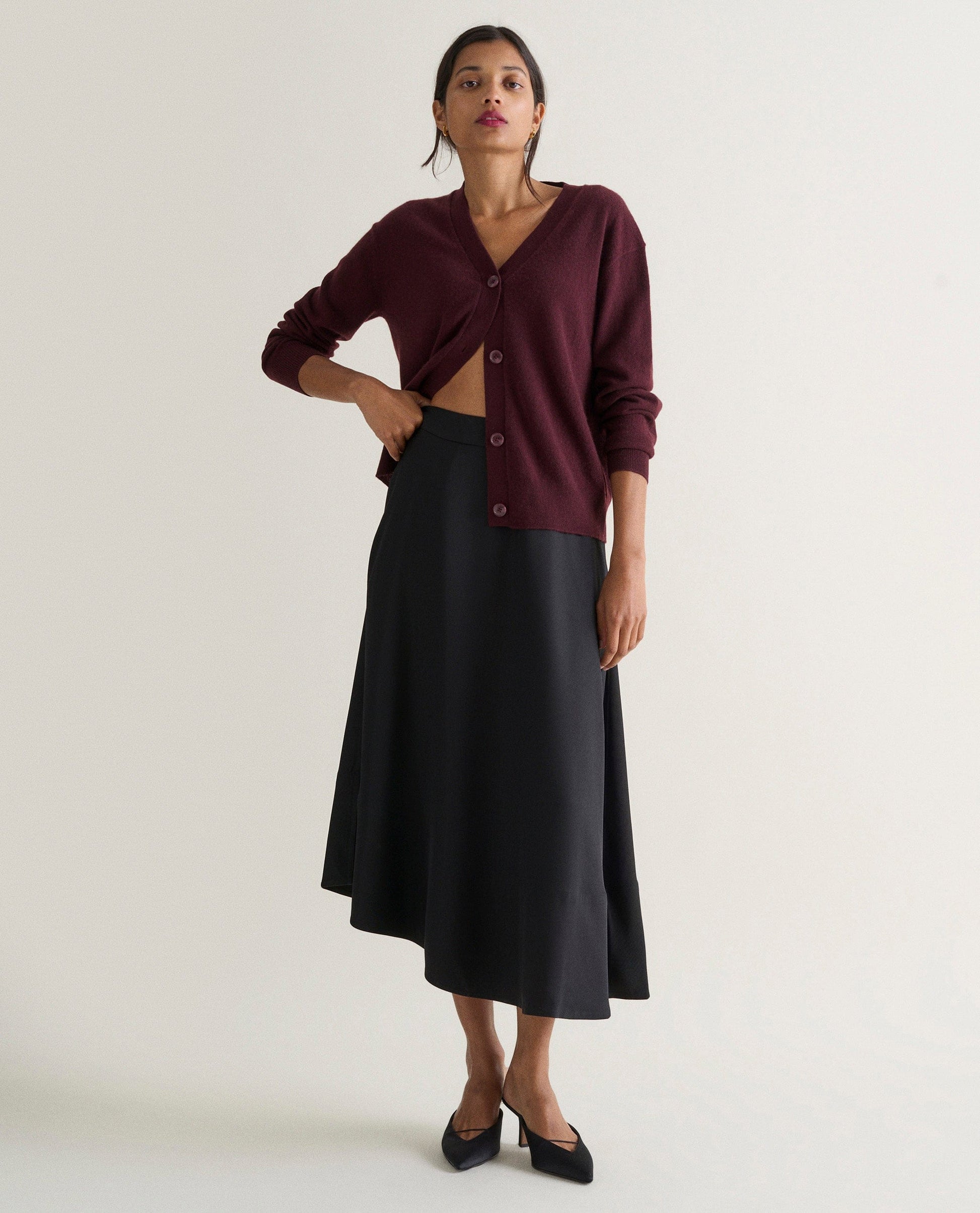 Image 1 of 4 showing woman wearing Rise & Fall's oxblood fine cashmere v-neck cardigan with black skirt.