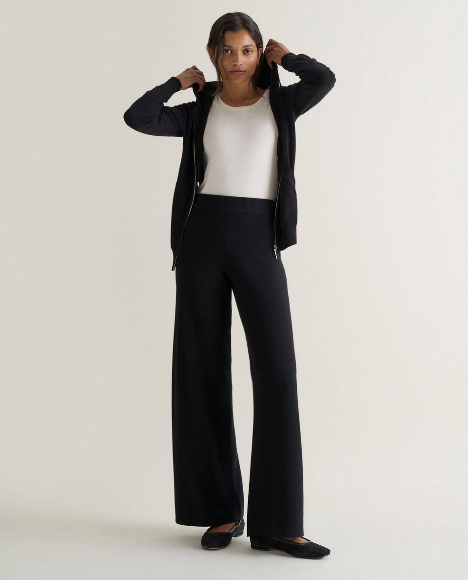 Image 1 of 4 showing woman wearing Rise & Fall's black fine cashmere wide-leg trousers with matching cashmere zip hoodie and a white t-shirt.