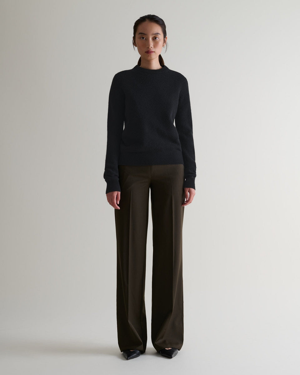 Image 1 of 4 showing woman wearing Rise & Fall's black mid-weight cashmere crew neck jumper with brown silk trousers.