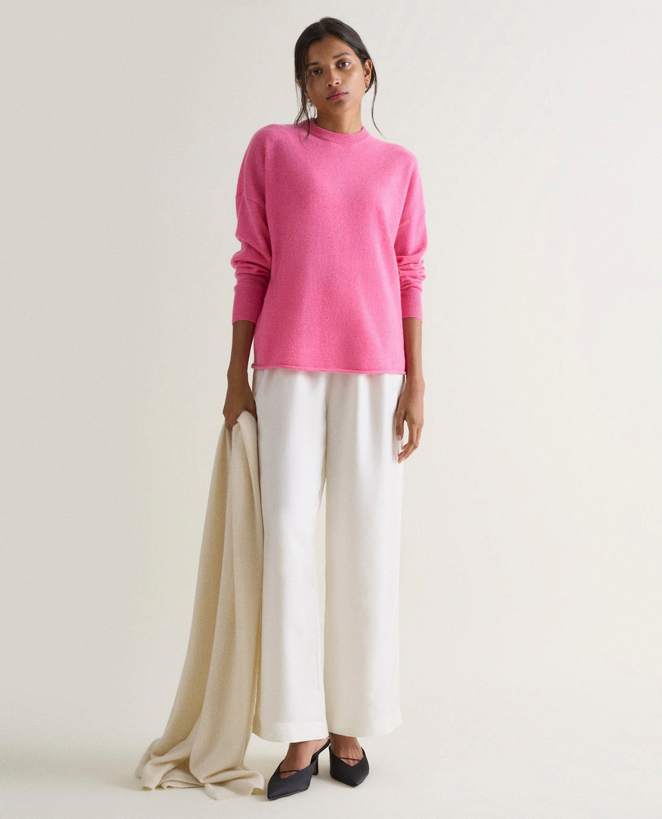 Image 1 of 4 showing woman wearing Rise & Fall's pink fine cashmere sweatshirt with white silk trousers.