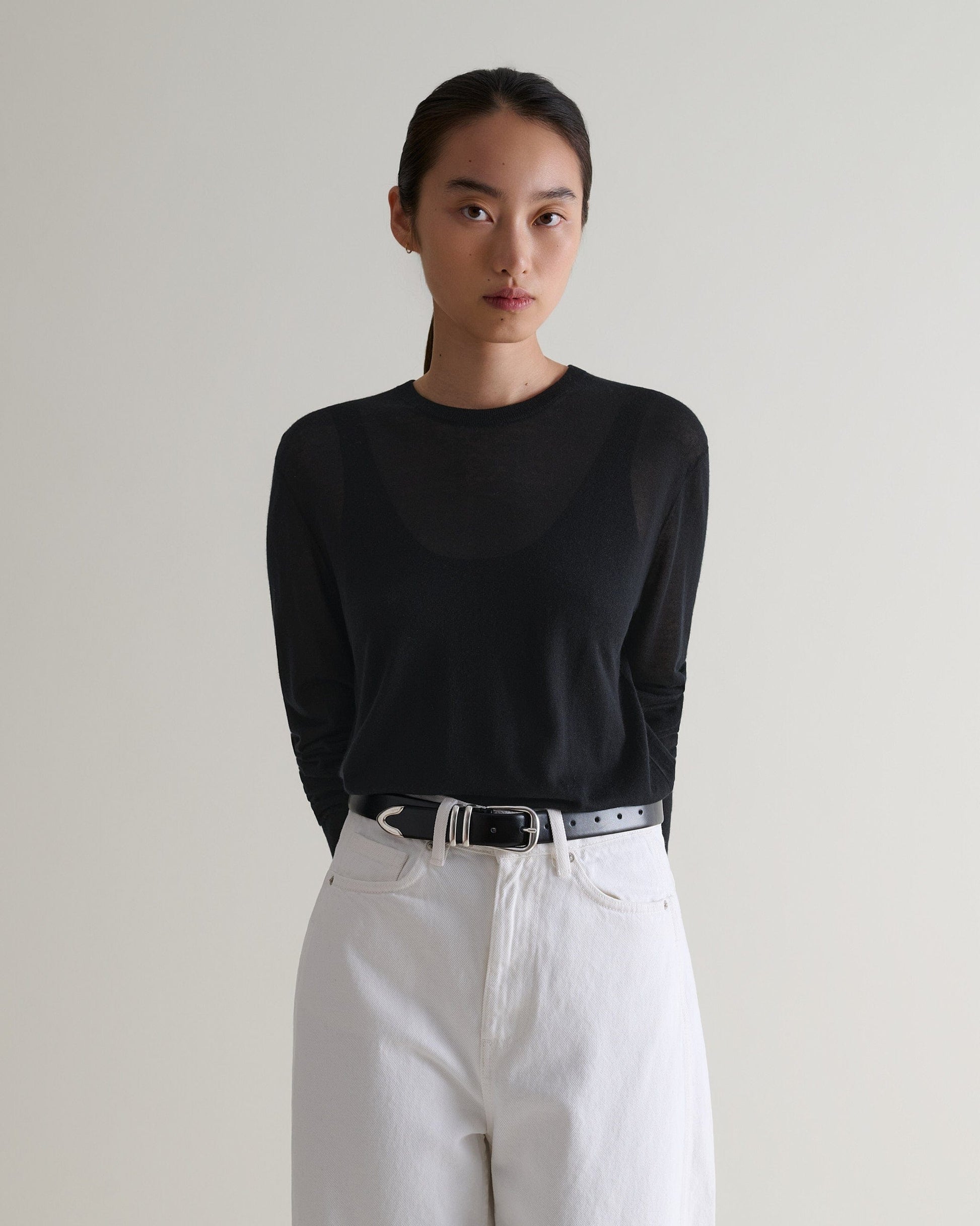 Image 1 of 5 showing woman wearing Rise & Fall's black tencel cashmere double layered crew neck jumper with white jeans, black belt.