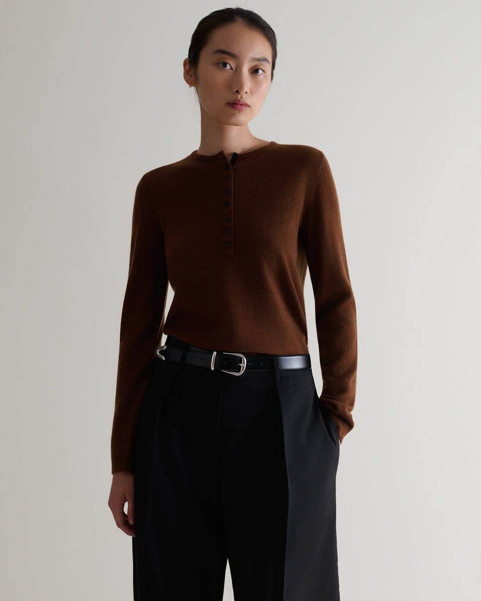 Image 1 of 5 showing a woman wearing Rise & Fall's brown cashmere merino henley jumper with black trousers and a black belt. 