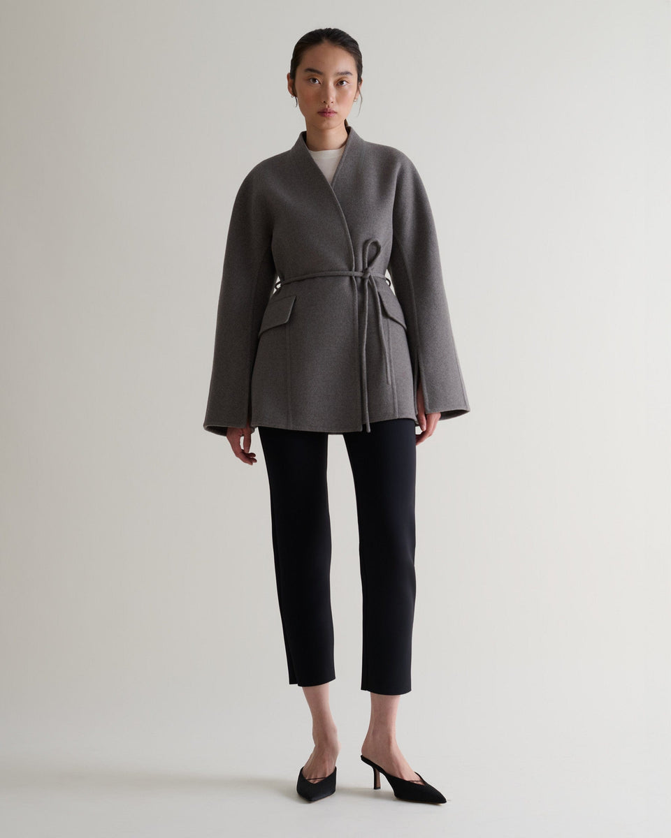 Image 1 of 5 showing woman wearing Rise & Fall's fawn cashmere wool double faced sculptural jacket with black cropped trousers.