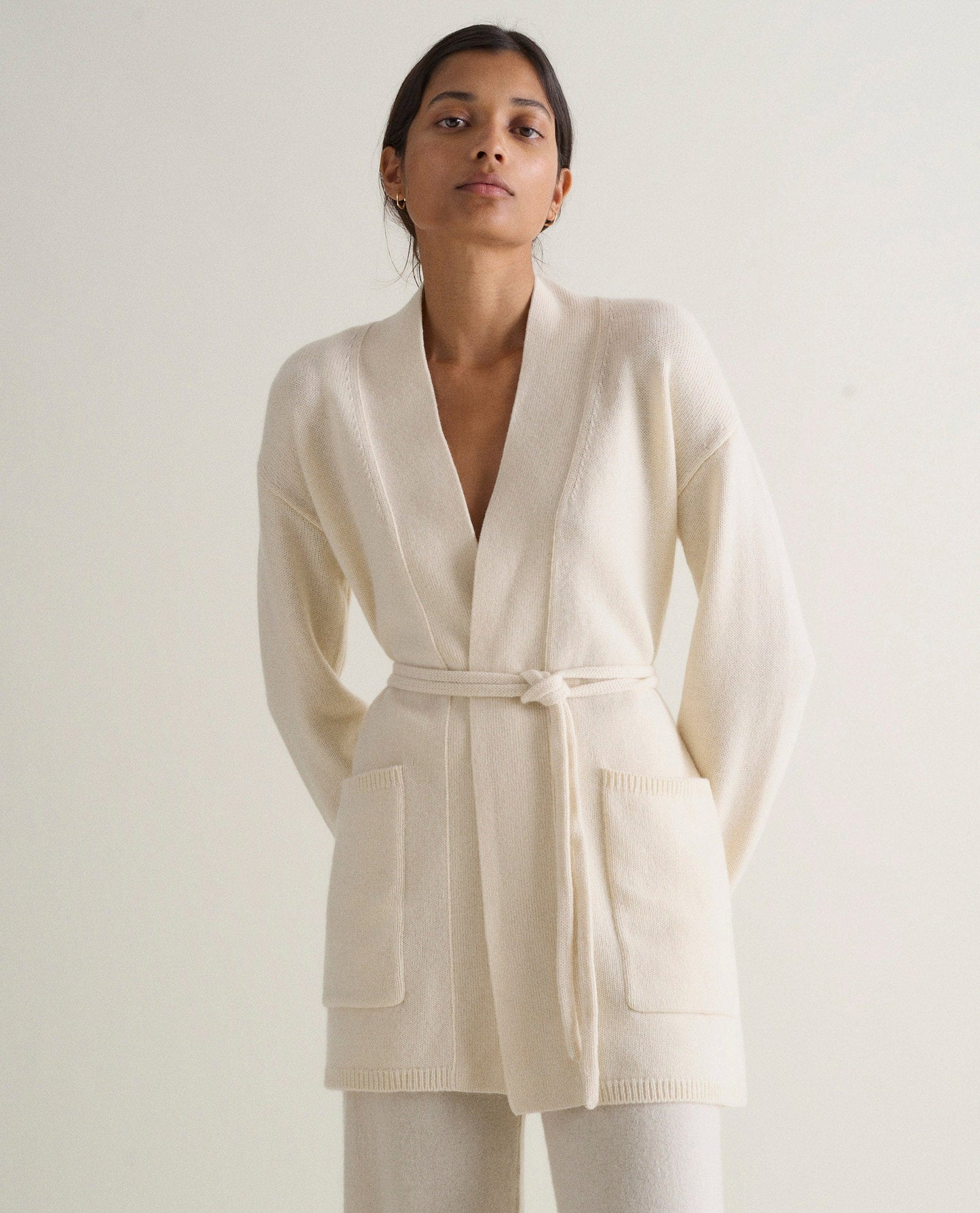 Image 1 of 5 showing woman wearing Rise & Fall's cream cashmere merino belted cardigan with matching cashmere trousers.