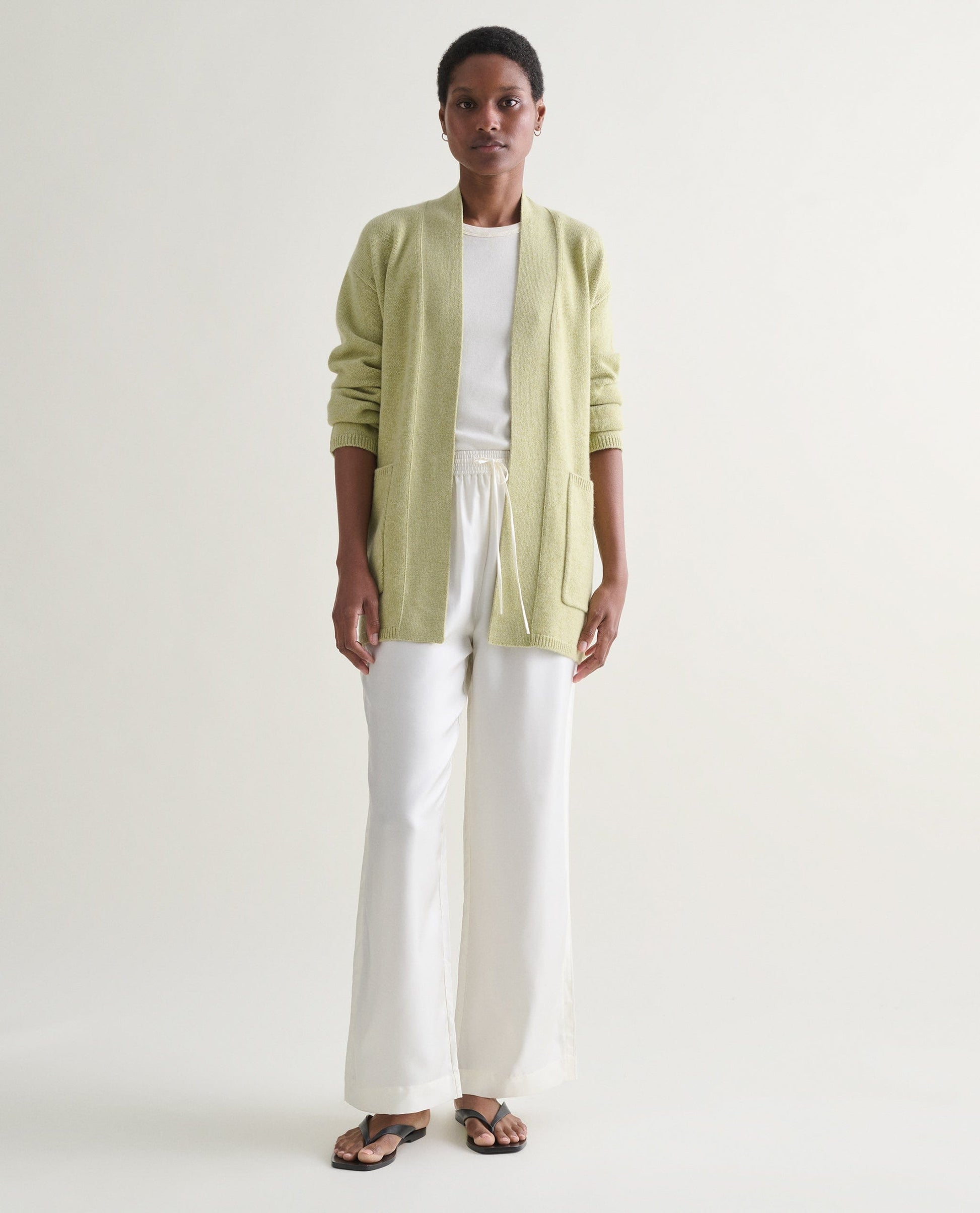 Image 1 of 5 showing woman wearing Rise & Fall's lichen green cashmere merino belted cardigan with white t-shirt and trousers.