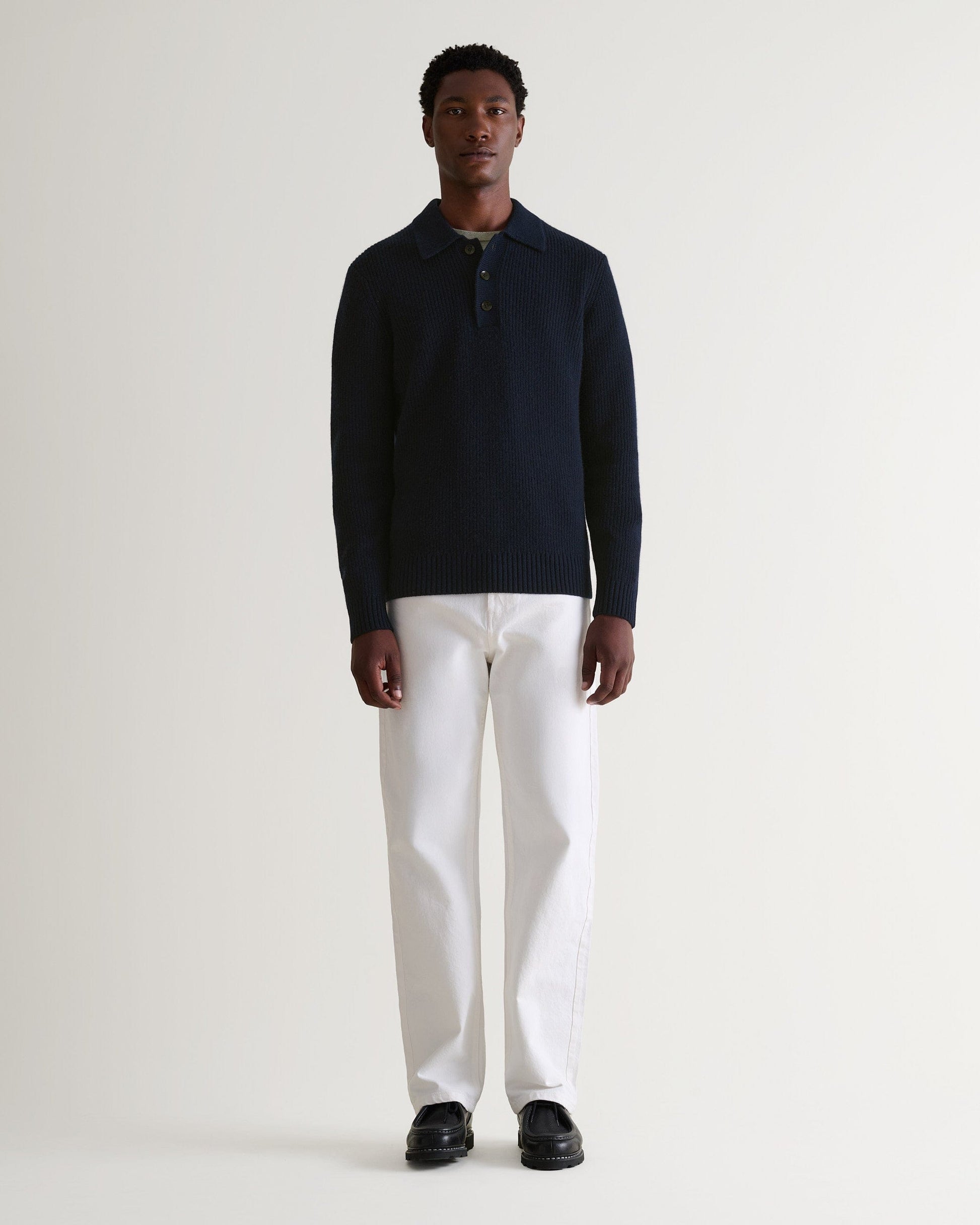 Image 1 of 6 showing man wearing Rise & Fall's navy cashmere merino fisherman ribbed polo sweater with white jeans and black shoes.