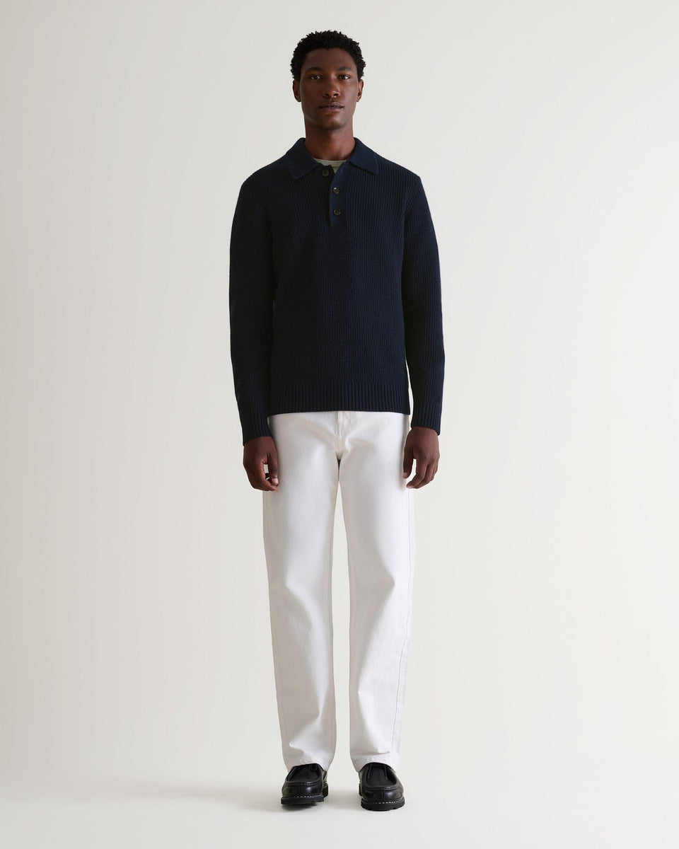 Image 1 of 6 showing man wearing Rise & Fall's navy cashmere merino fisherman ribbed polo sweater with white jeans and black shoes.