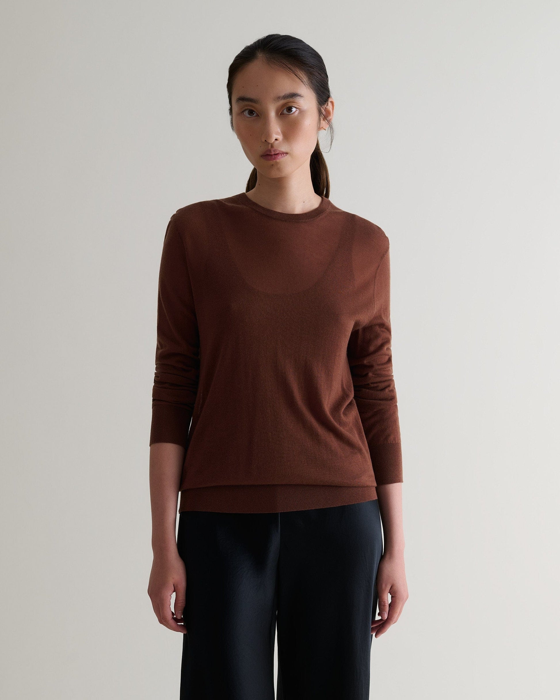 Image 1 of 6 showing woman wearing Rise & Fall's brown tencel cashmere double layered crew neck jumper with black trousers. 