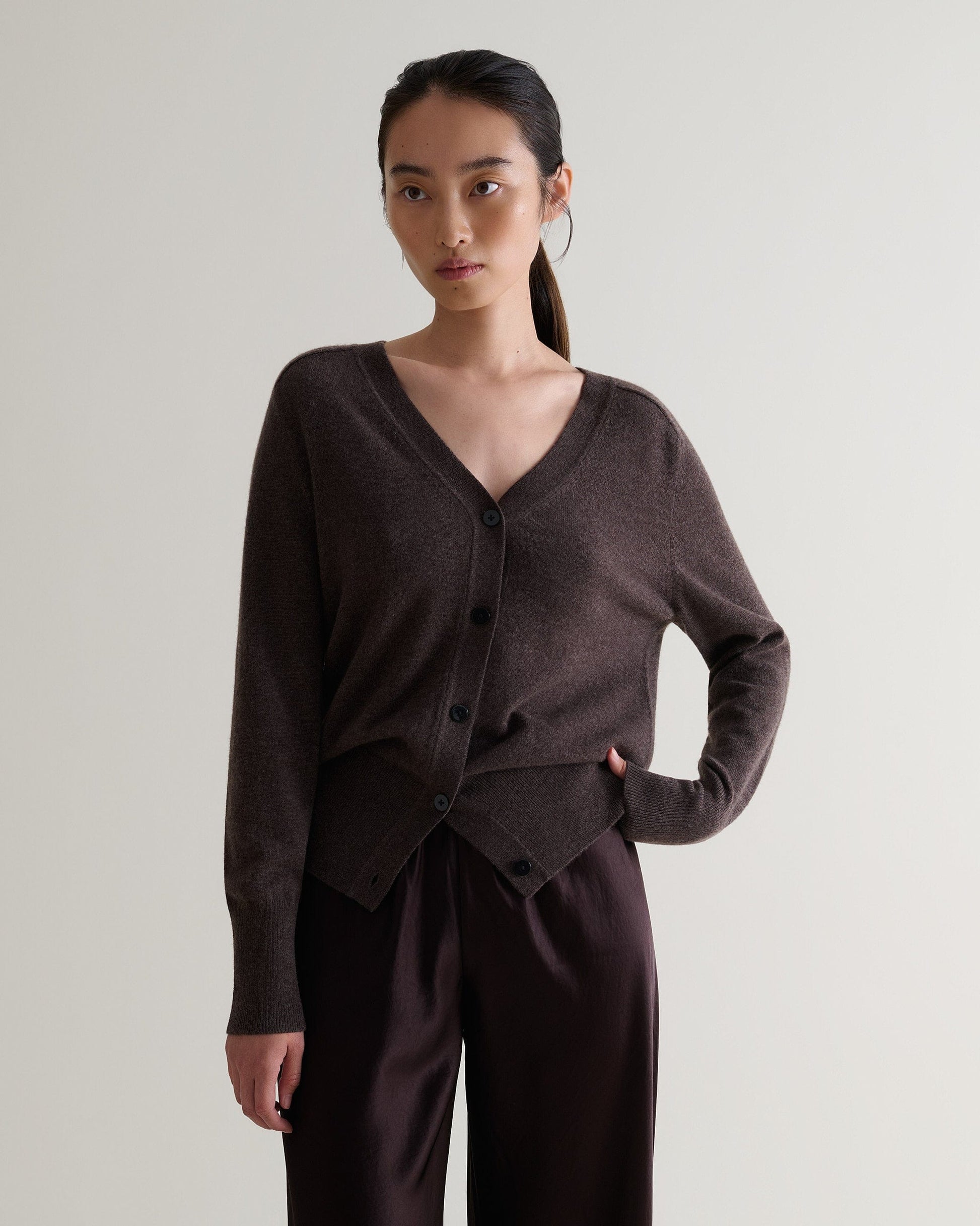 Image 1 of 6 showing woman wearing Rise & Fall's chocolate fine cashmere blouson cardigan with silk brown trousers.