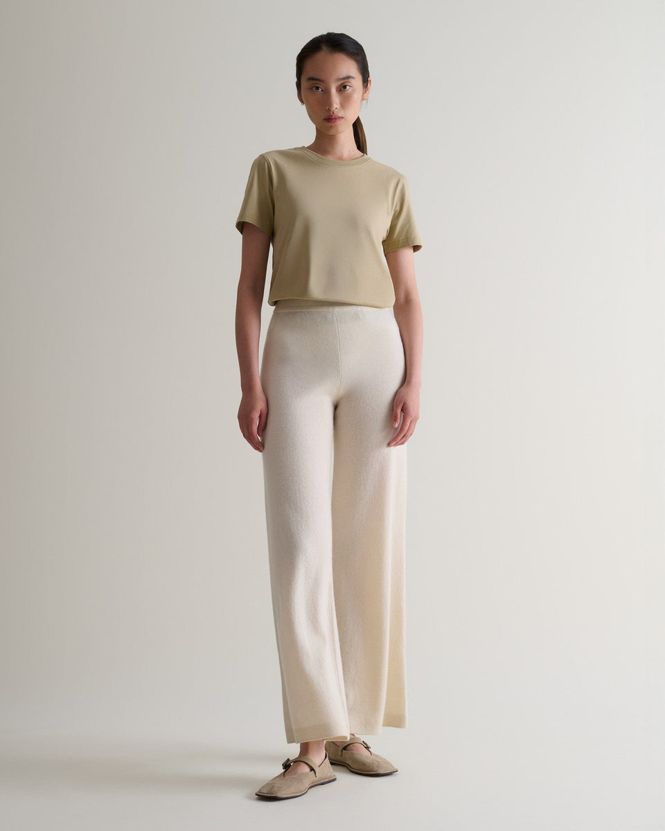 Image 1 of 6 showing woman wearing Rise & Fall's cream fine cashmere wide-leg trousers with beige t-shirt and shoes.