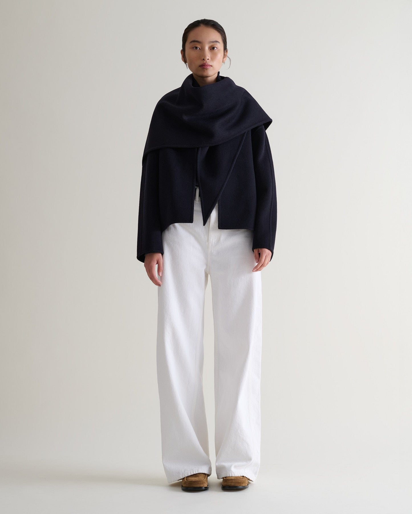 Image 1 of 7 showing woman wearing Rise & Fall's navy cashmere wool double faced scarf jacket with white jeans.