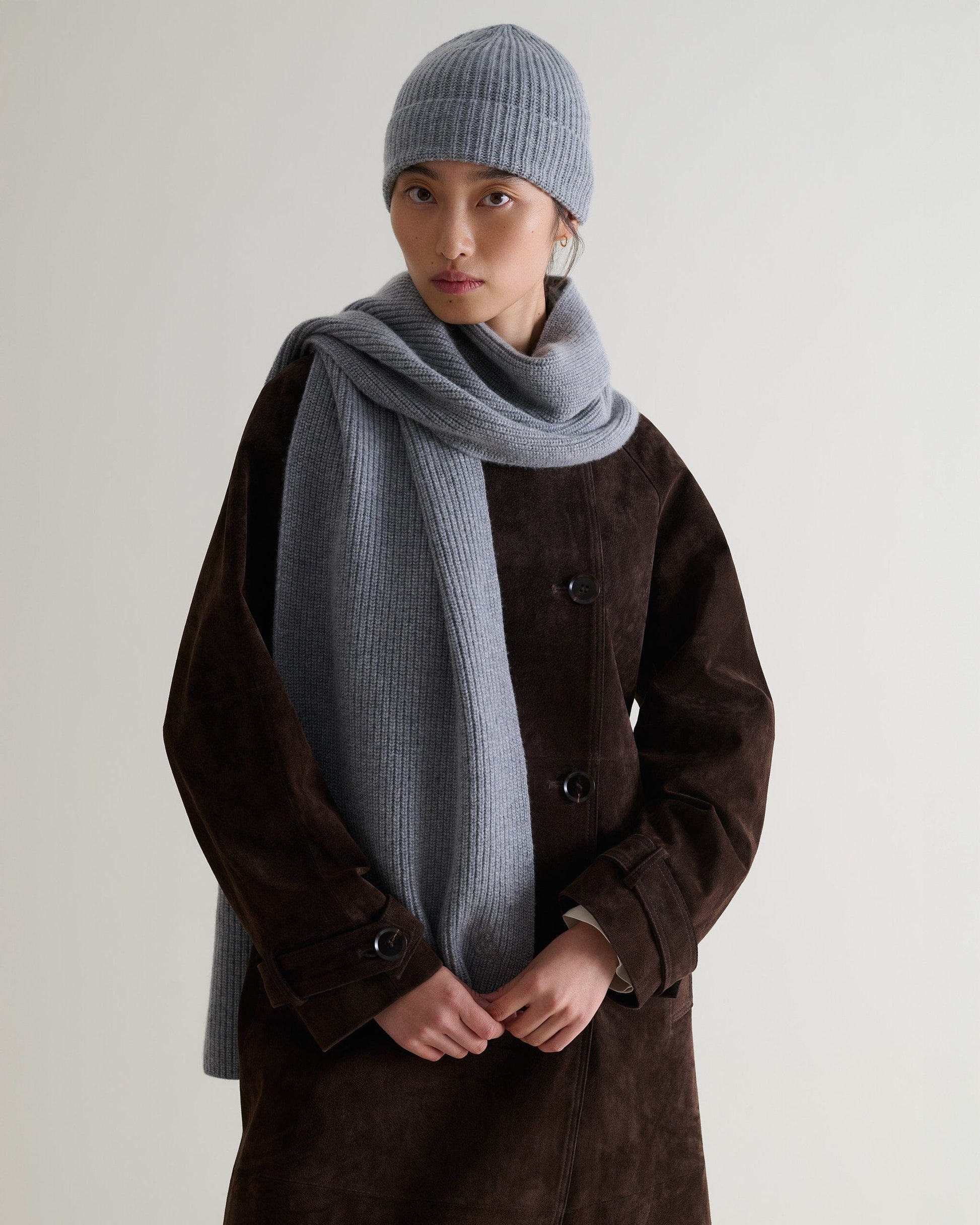 Image 2 of 2 shows woman wearing Rise & Fall's grey cashmere merino ribbed scarf and beanie with chocolate suede coat