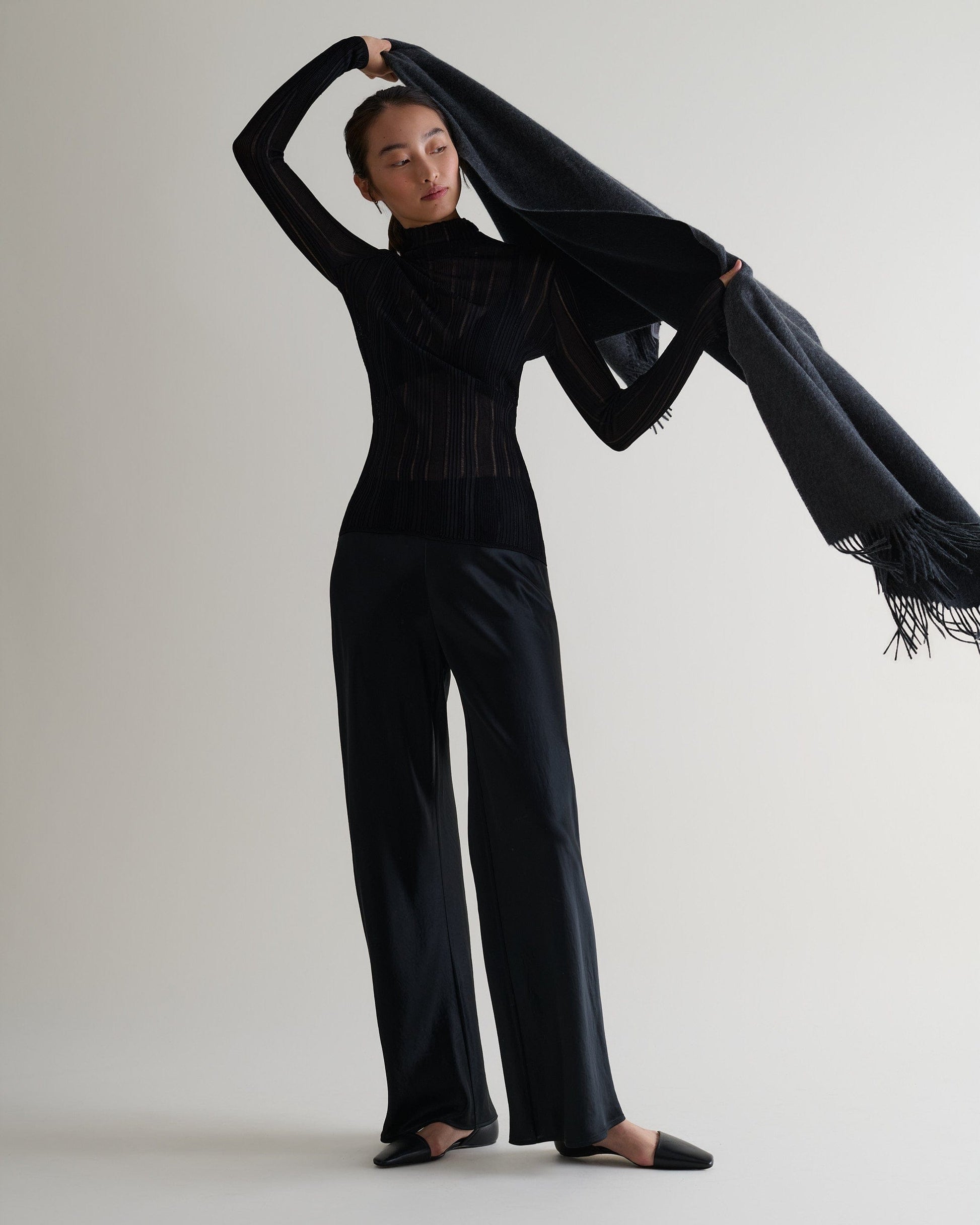 Image 2 of 5 showing woman drapping Rise & Fall's finest cashmere double faced wrap over shoulders, colour: charcoal and black.