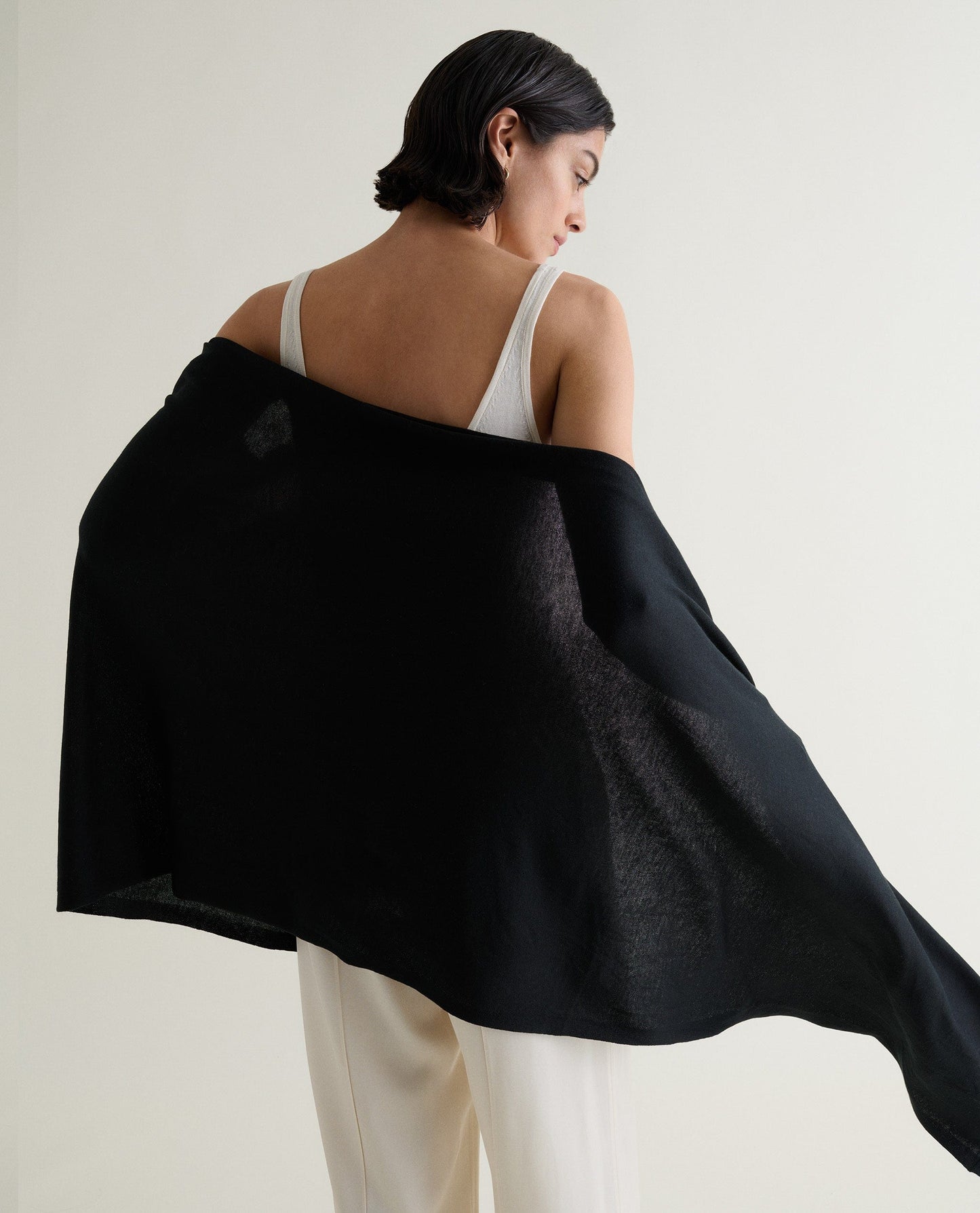 Image 2 of 5 showing back view of woman wrapping Rise & Fall's black oversized cashmere scarf around her.