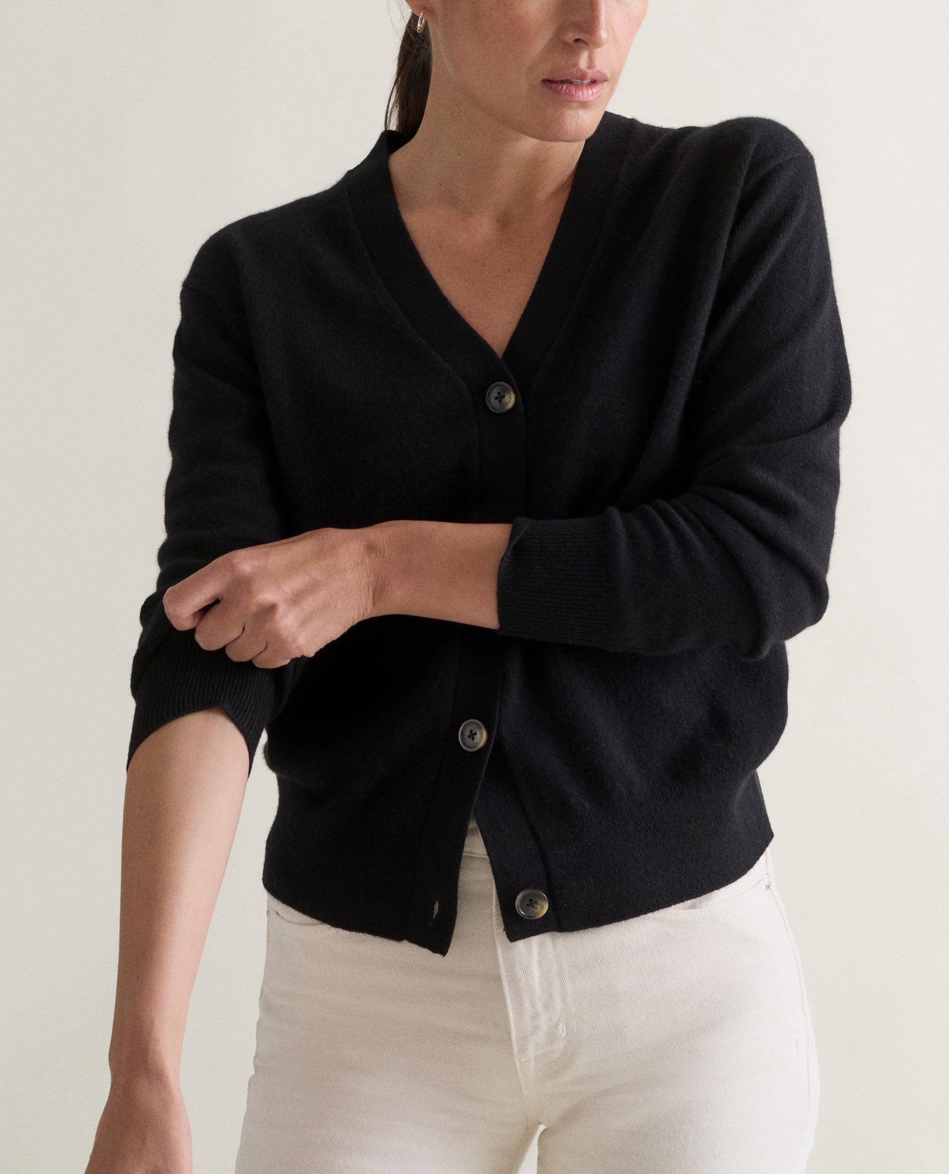 Image 3 of 3 showing woman wearing Rise & Fall's black fine cashmere v-neck cardigan with white jeans.
