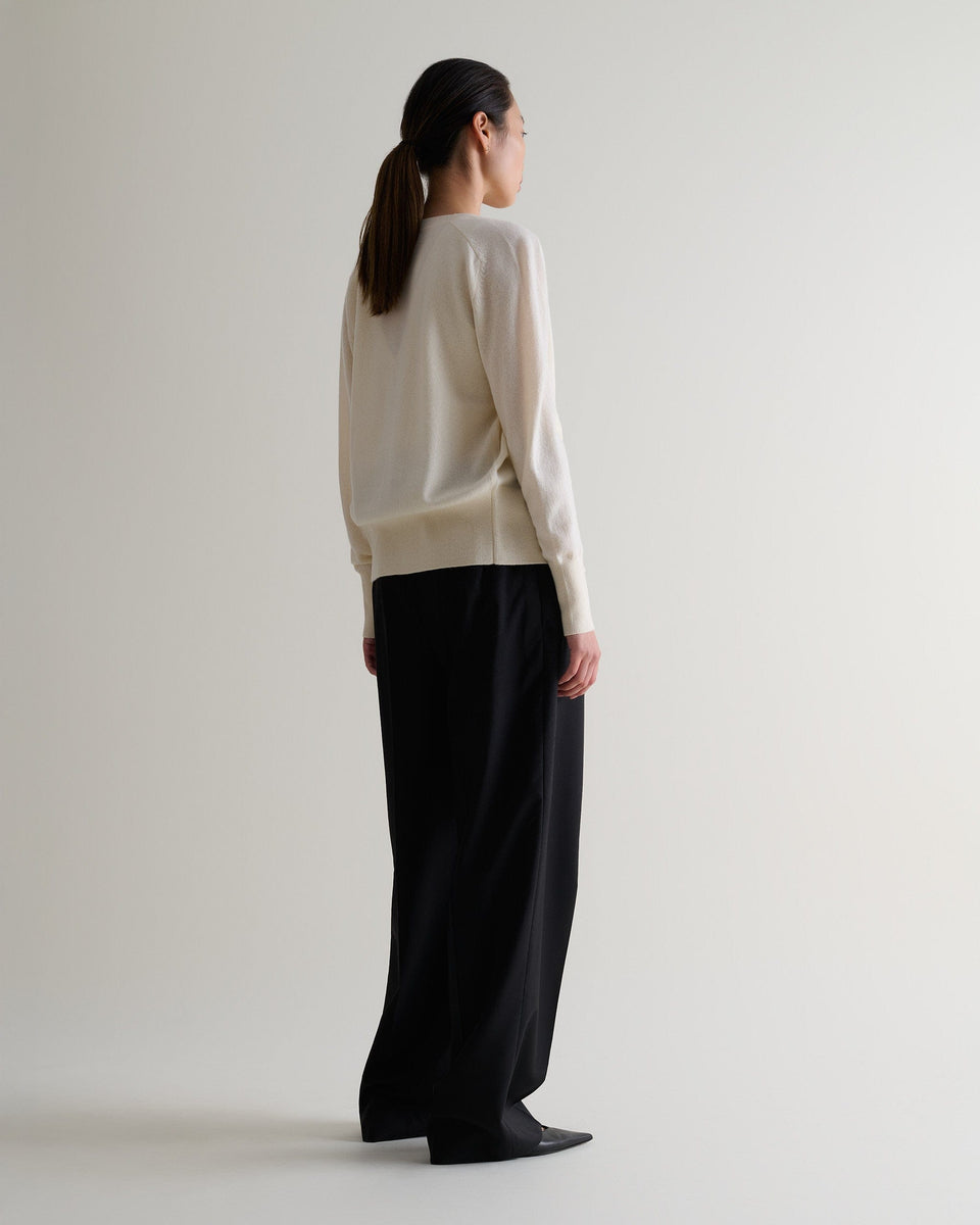 Image 3 of 3 showing back of woman wearing Rise & Fall's buttermilk fine cashmere blouson cardigan with matching top and black wide leg trousers.