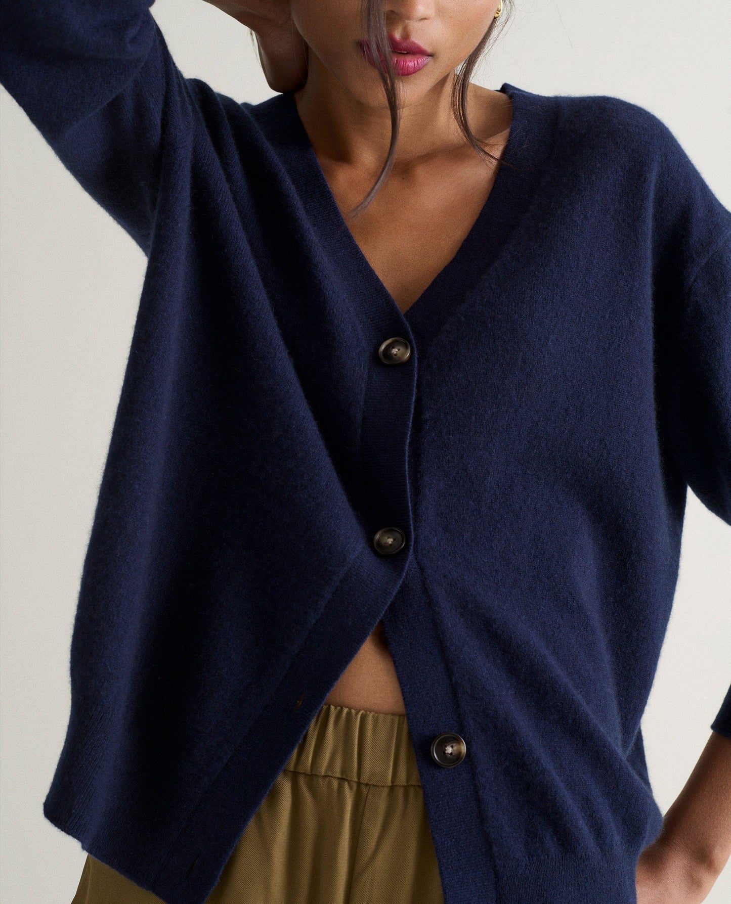 Image 3 of 4 showing woman wearing Rise & Fall's navy fine cashmere v-neck cardigan with olive trousers.