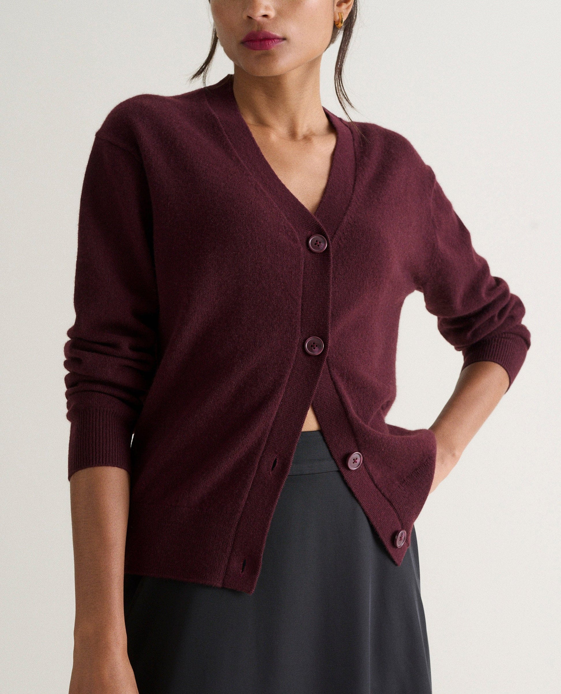 Image 3 of 4 showing woman wearing Rise & Fall's oxblood fine cashmere v-neck cardigan with black skirt.