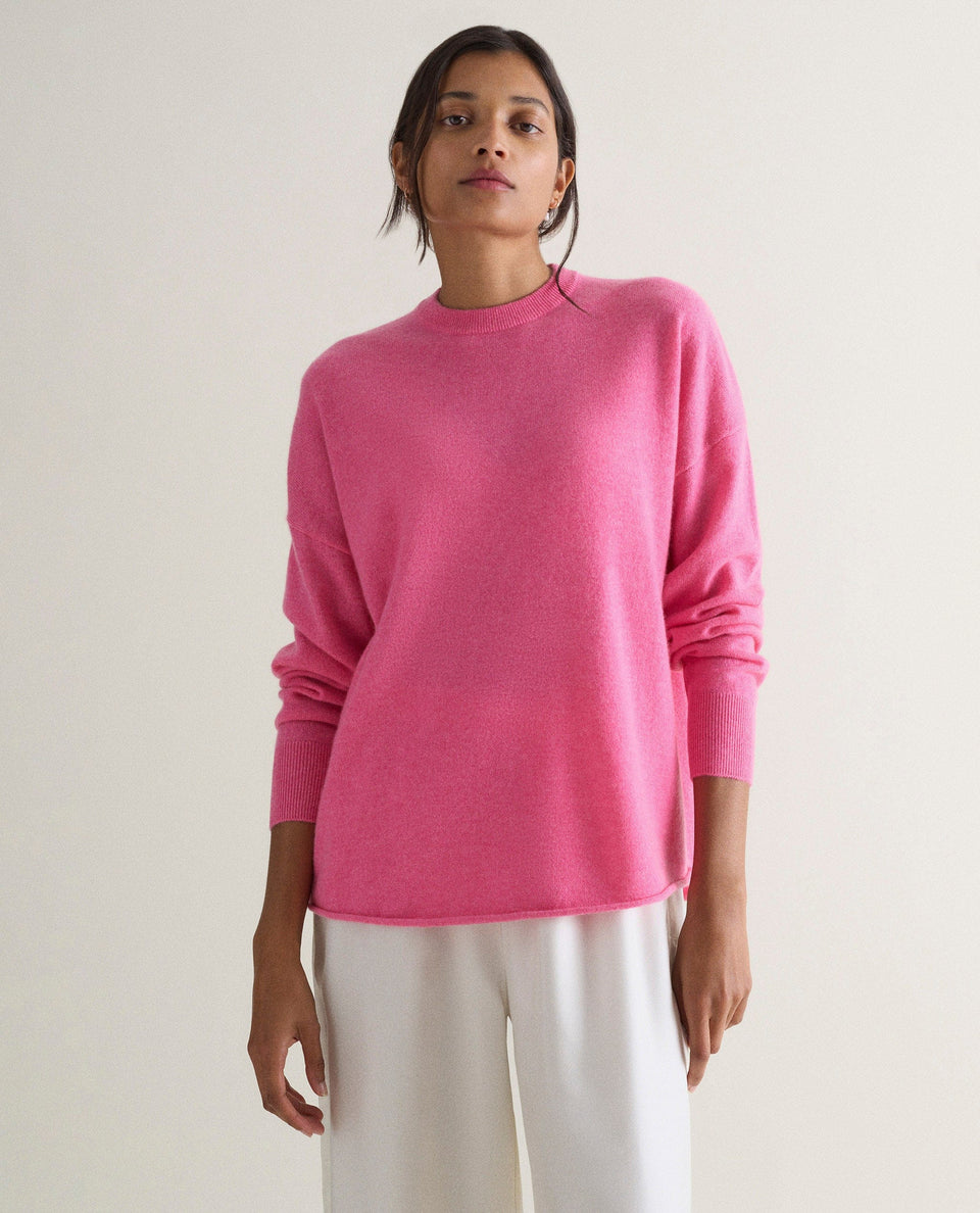 Image 3 of 4 showing woman wearing Rise & Fall's pink fine cashmere sweatshirt with white silk trousers.
