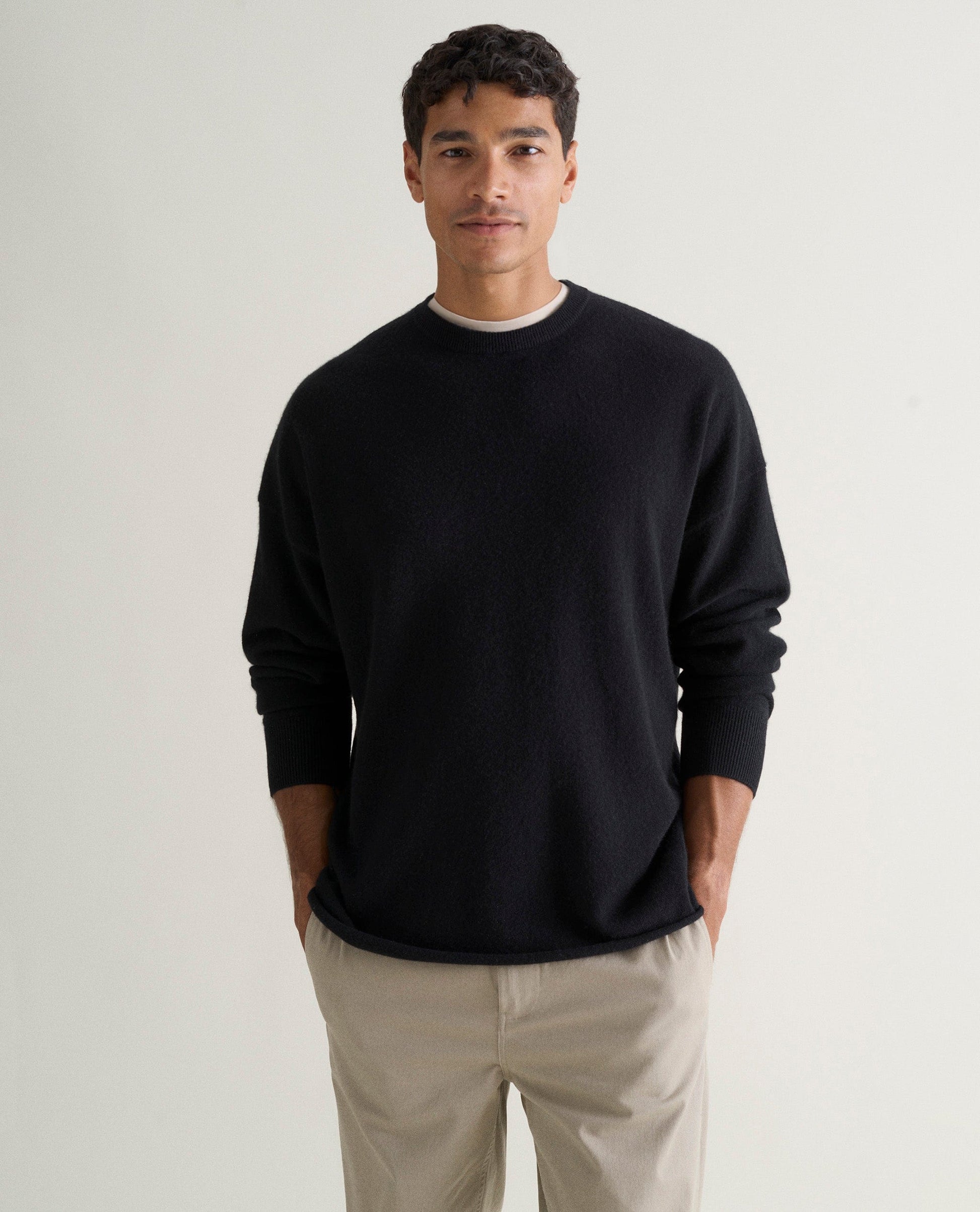 Image 3 of 5 showing man wearing Rise & Fall's black finest cashmere sweatshirt over white T-shirt and stone-coloured trousers.