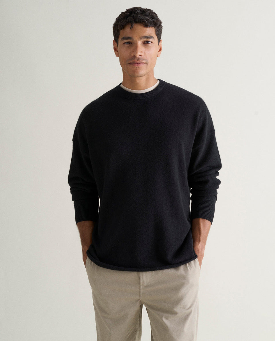Image 3 of 5 showing man wearing Rise & Fall's black finest cashmere sweatshirt over white T-shirt and stone-coloured trousers.