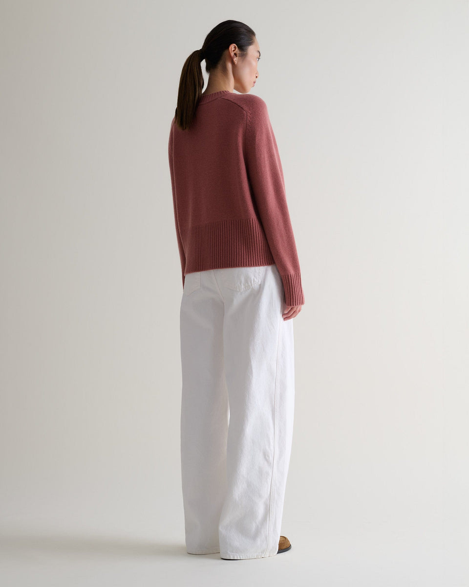 Image 3 of 5 showing back of woman wearing Rise & Fall pink clay cashmere merino saddle sleeve crew neck jumper with white ide leg jeans.