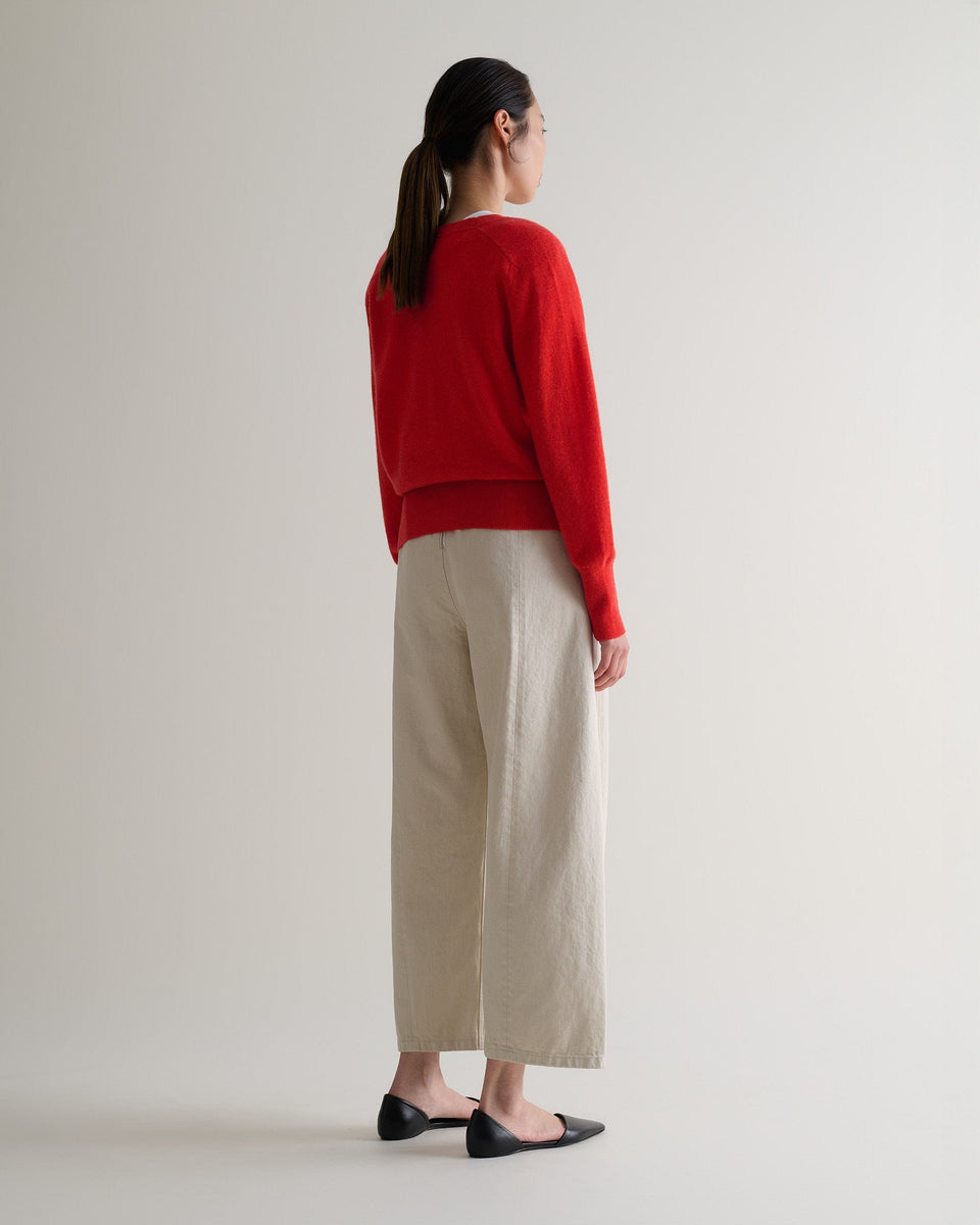 Image 3 of 5 showing back of woman wearing Rise & Fall's poppy red fine cashmere blouson cardigan with cream trousers.