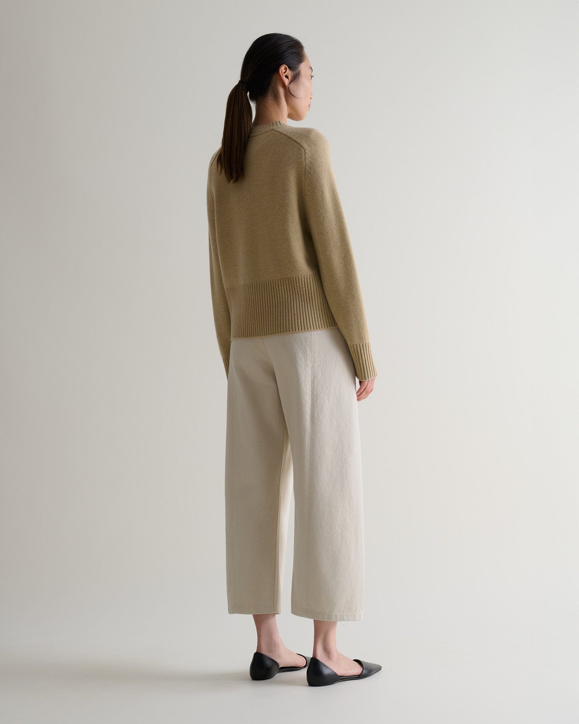 Image 3 of 5 showing back of woman wearing Rise & Fall twine cashmere merino saddle sleeve crew neck jumper with cream barrel jeans.