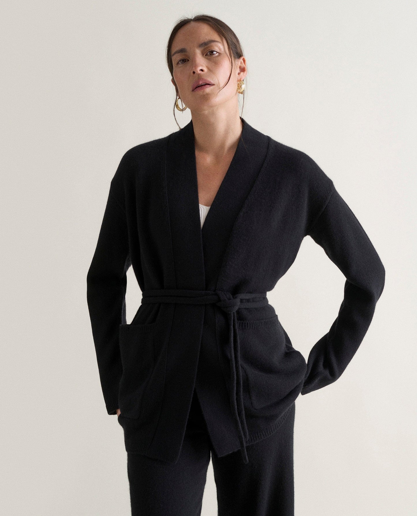 Image 3 of 5 showing woman wearing Rise & Fall's black cashmere merino belted cardigan with black trousers and white top.