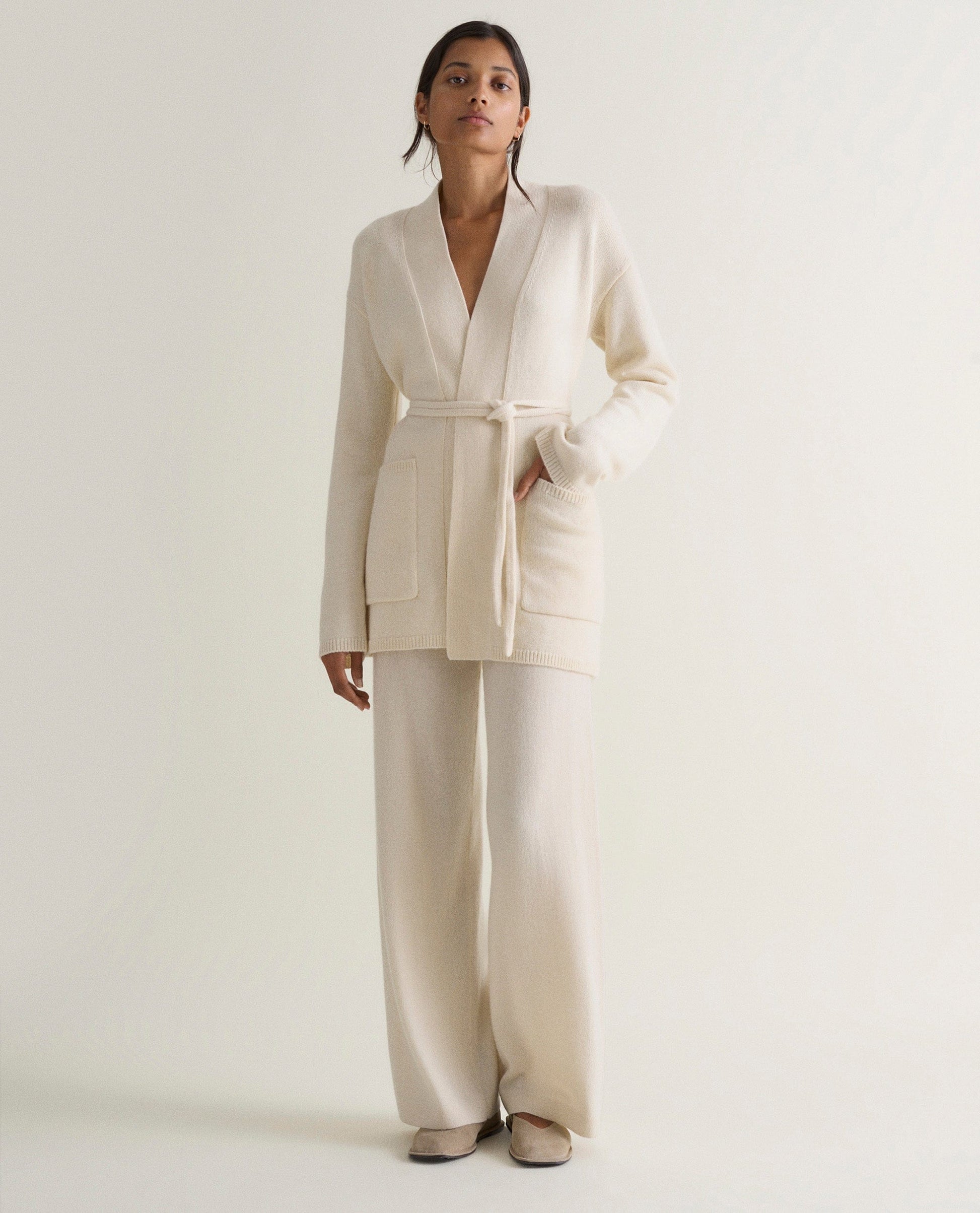 Image 3 of 5 showing woman wearing Rise & Fall's cream cashmere merino belted cardigan with matching cashmere trousers.