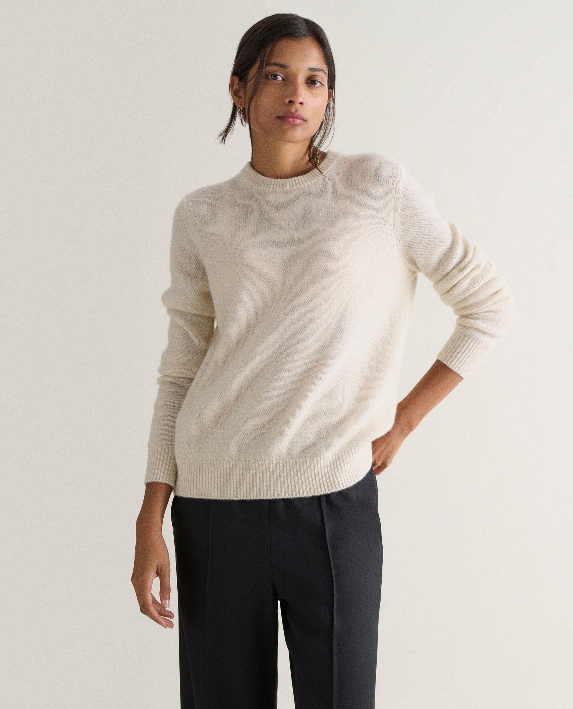Image 3 of 5 showing woman wearing Rise & Fall's cream mid-weight cashmere crew neck jumper with black trousers.