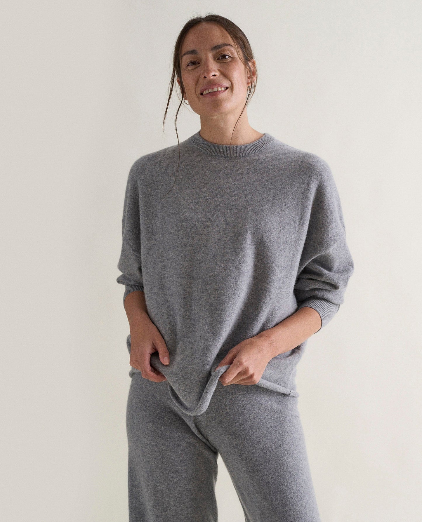 Image 3 of 5 showing woman wearing Rise & Fall's grey fine cashmere sweatshirt with matching cashmere trousers.