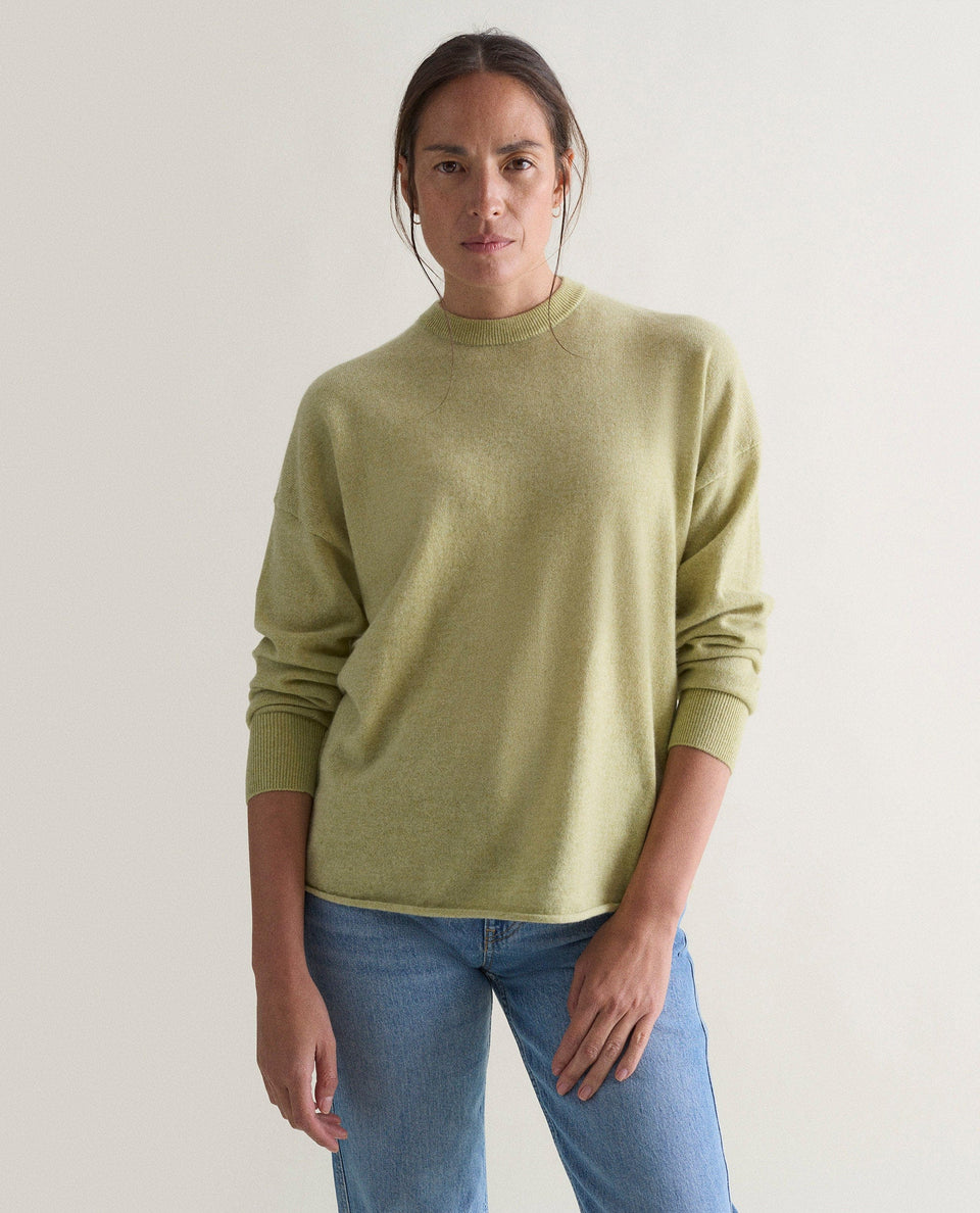 Image 3 of 5 showing woman wearing Rise & Fall's lichen green fine cashmere sweatshirt with pale blue jeans.