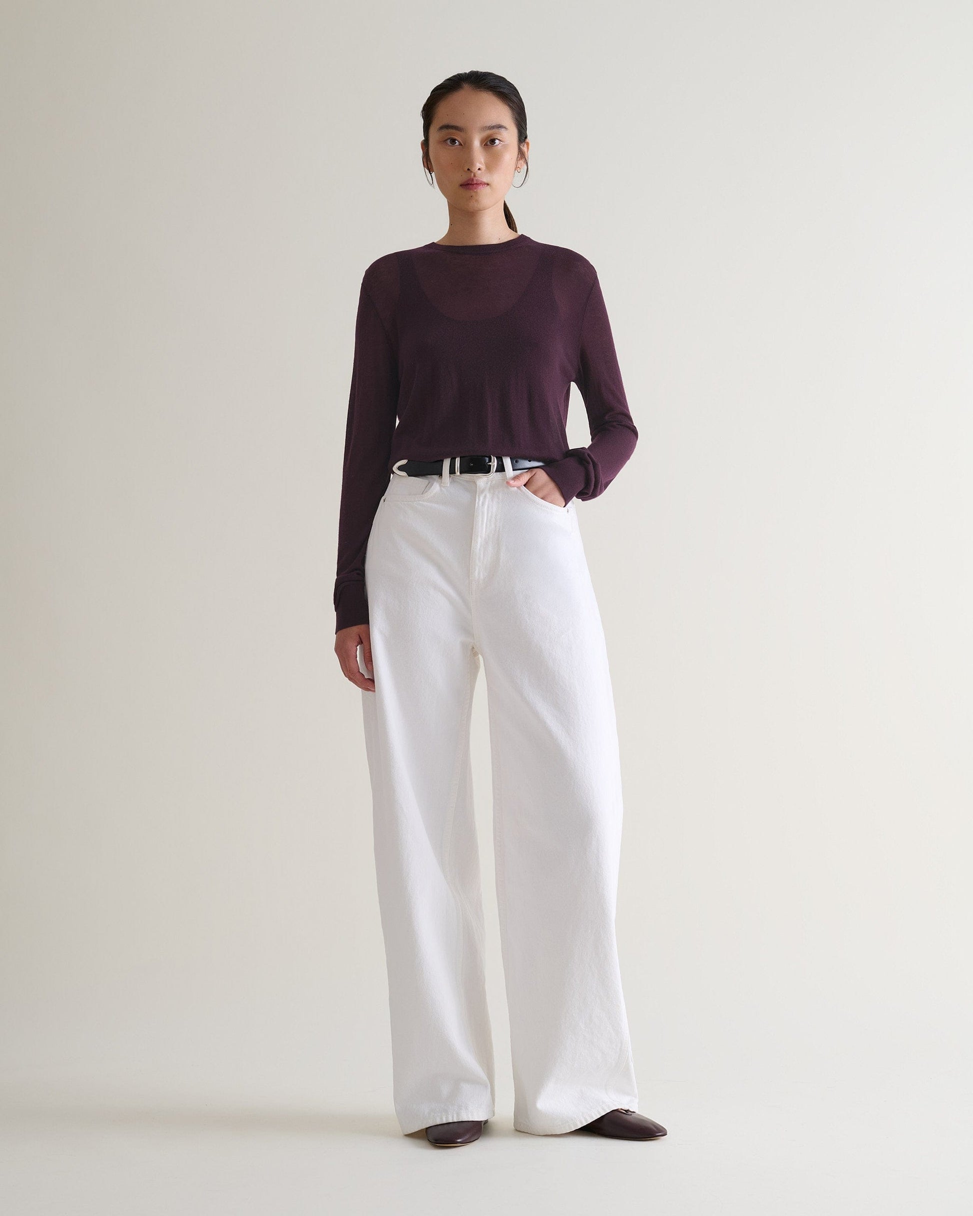 Image 3 of 5 showing a woman wearing Rise & Fall's oxblood tencel™ cashmere double layered crew neck jumper with white jeans and black leather belt. 
