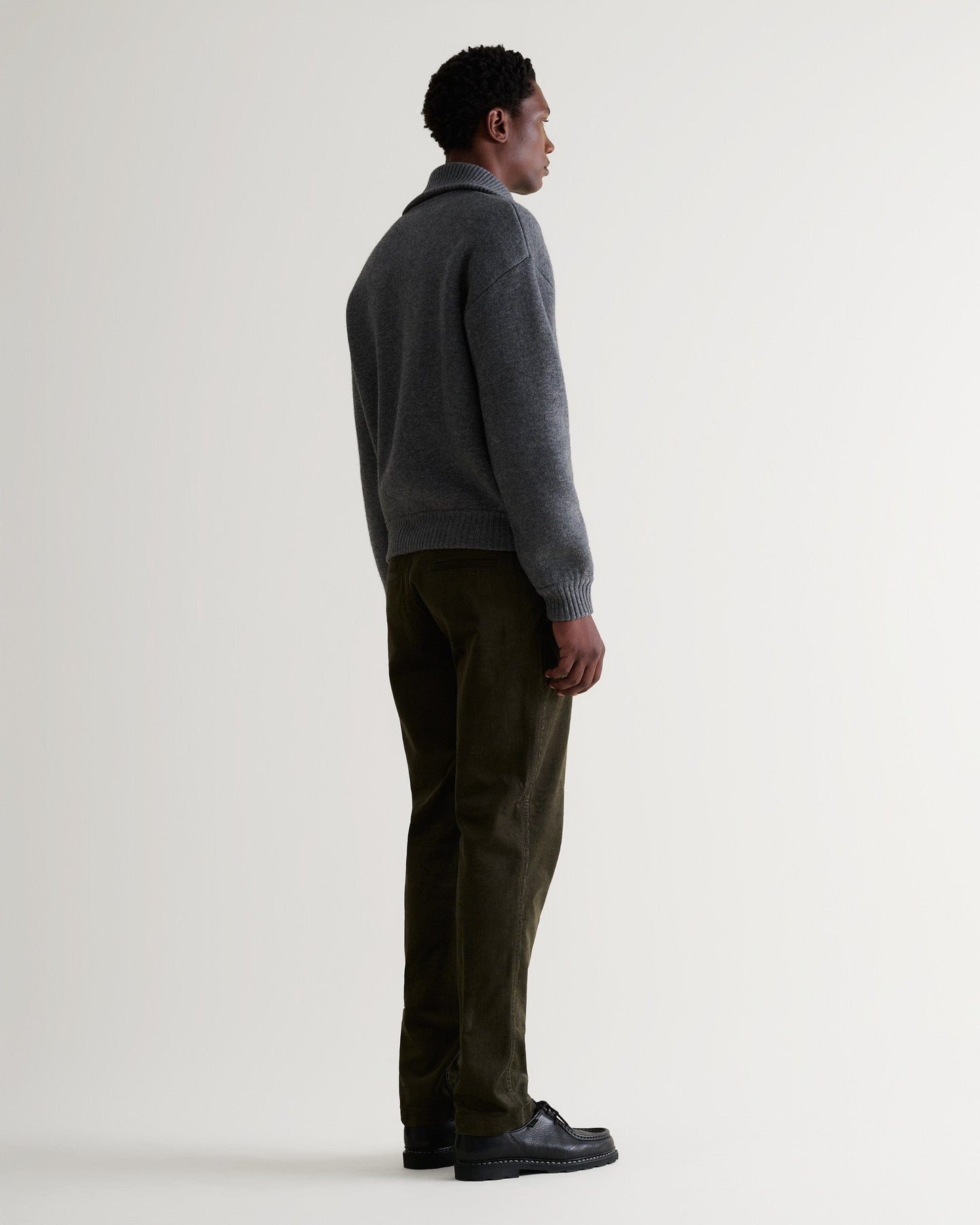 Image 3 of 6 showing man wearing Rise & Fall's dark grey cashmere merino buttoned knitted bomber with green corduroy trousers.