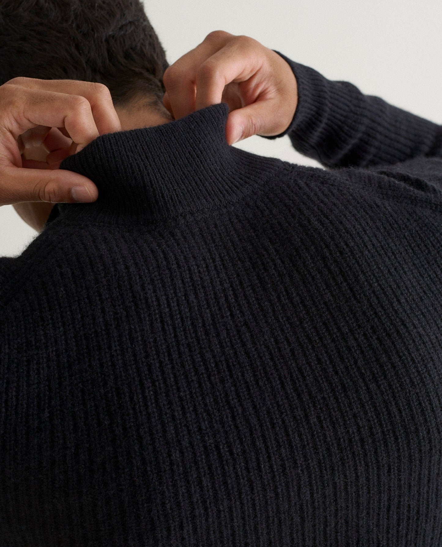 Image 3 of 6 showing back of man wearing Rise & Fall's Cashmere Merino Fishermans Rib 1/4 Zip Jumper in black.