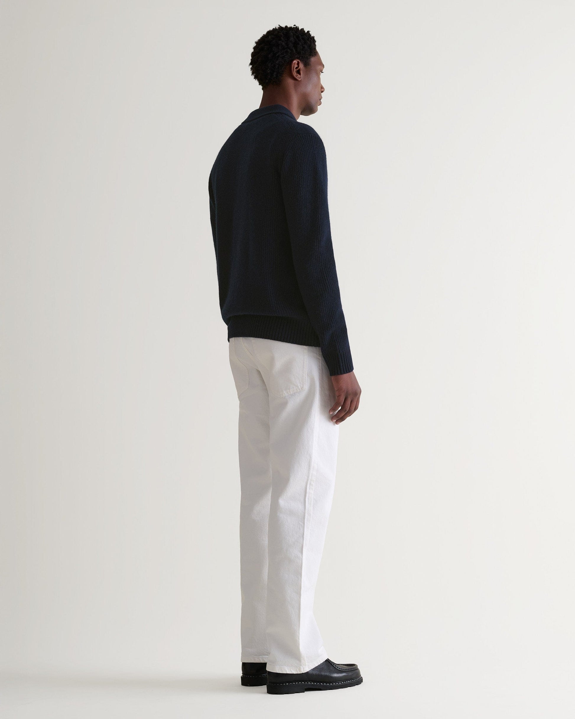 Image 3 of 6 showing man wearing Rise & Fall's graphite cashmere merino fisherman ribbed polo jumper with white T-Shirt and black trousers