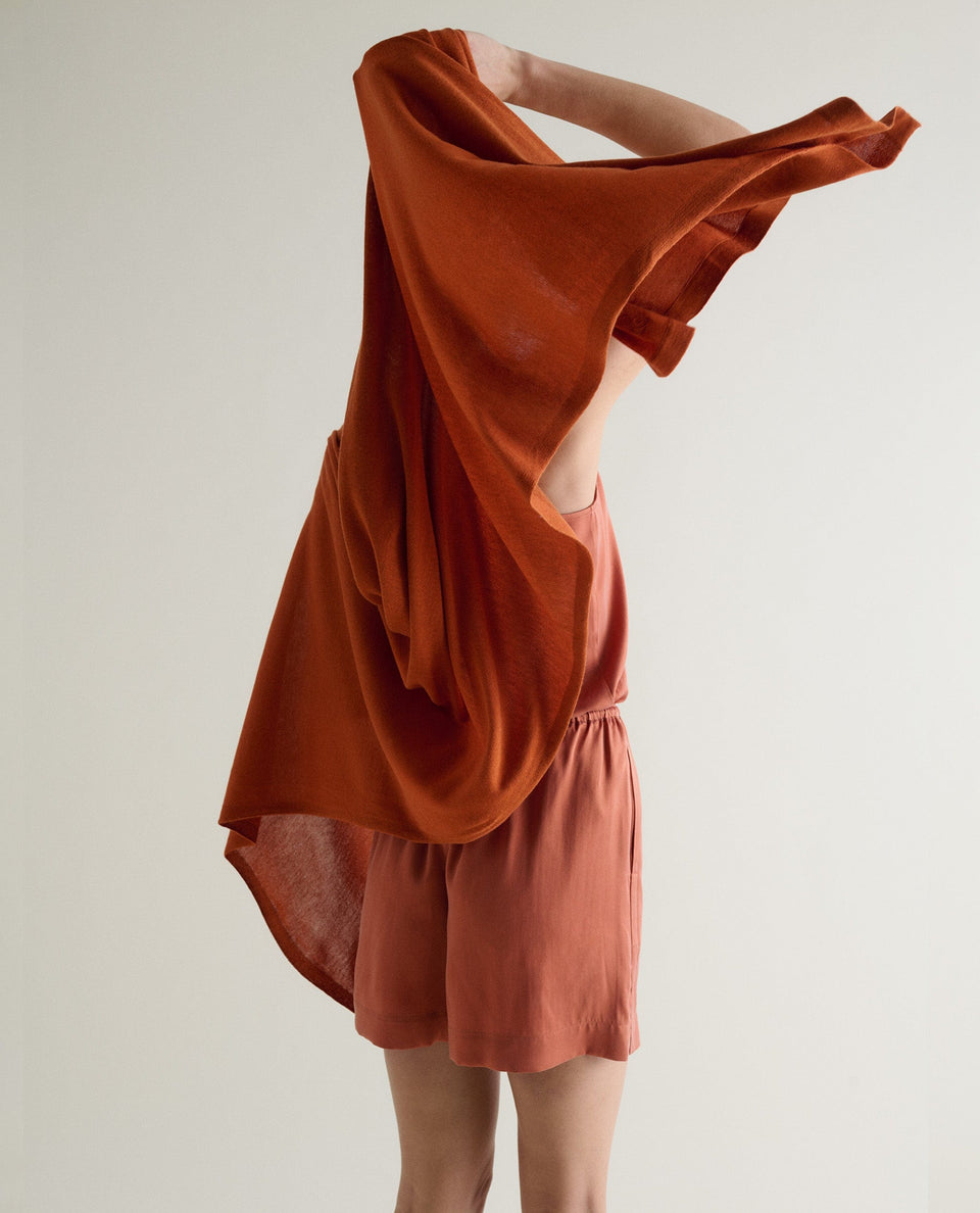 Image 3 of 6 showing woman drapping Rise & Fall's rust oversized cashmere scarf around shoulders, back view.