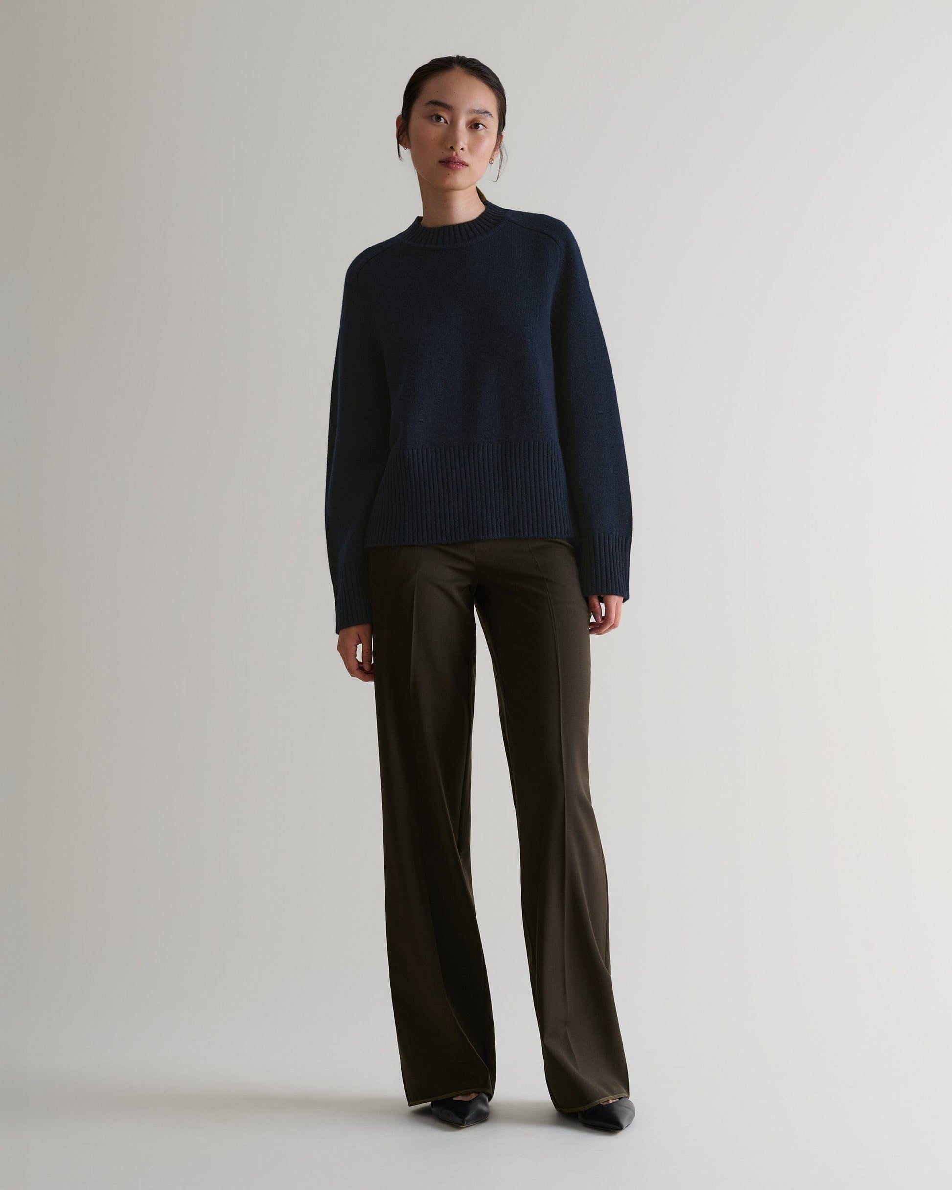 Image 3 of 6 showing woman wearing Rise & Fall indigo cashmere merino saddle sleeve crew neck jumper with brown trousers.