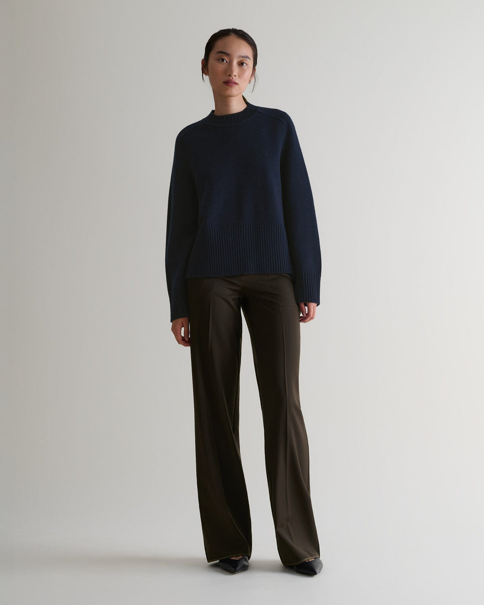 Image 3 of 6 showing woman wearing Rise & Fall indigo cashmere merino saddle sleeve crew neck jumper with brown trousers.