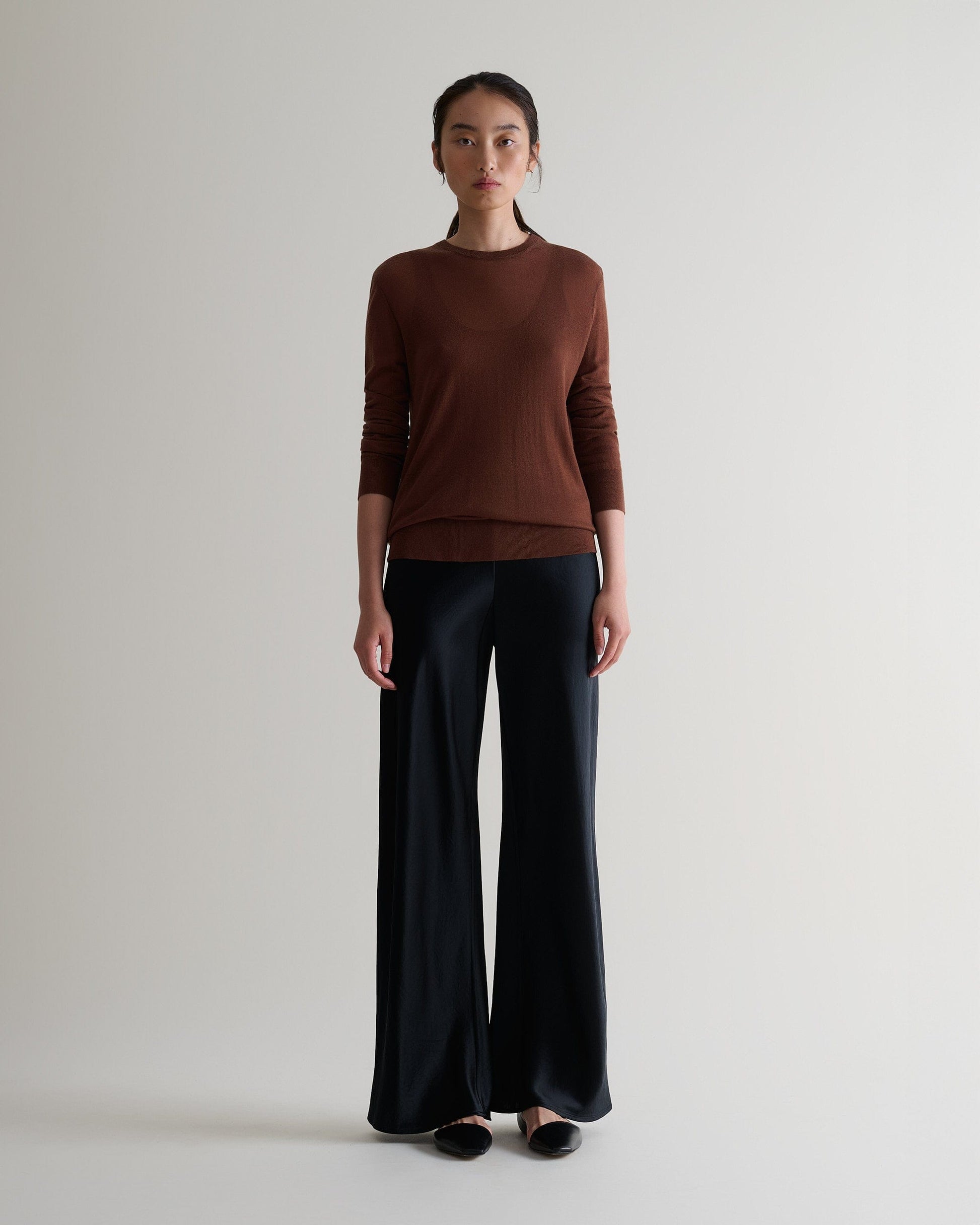 Image 3 of 6 showing woman wearing Rise & Fall's brown tencel cashmere double layered crew neck jumper with black trousers. 